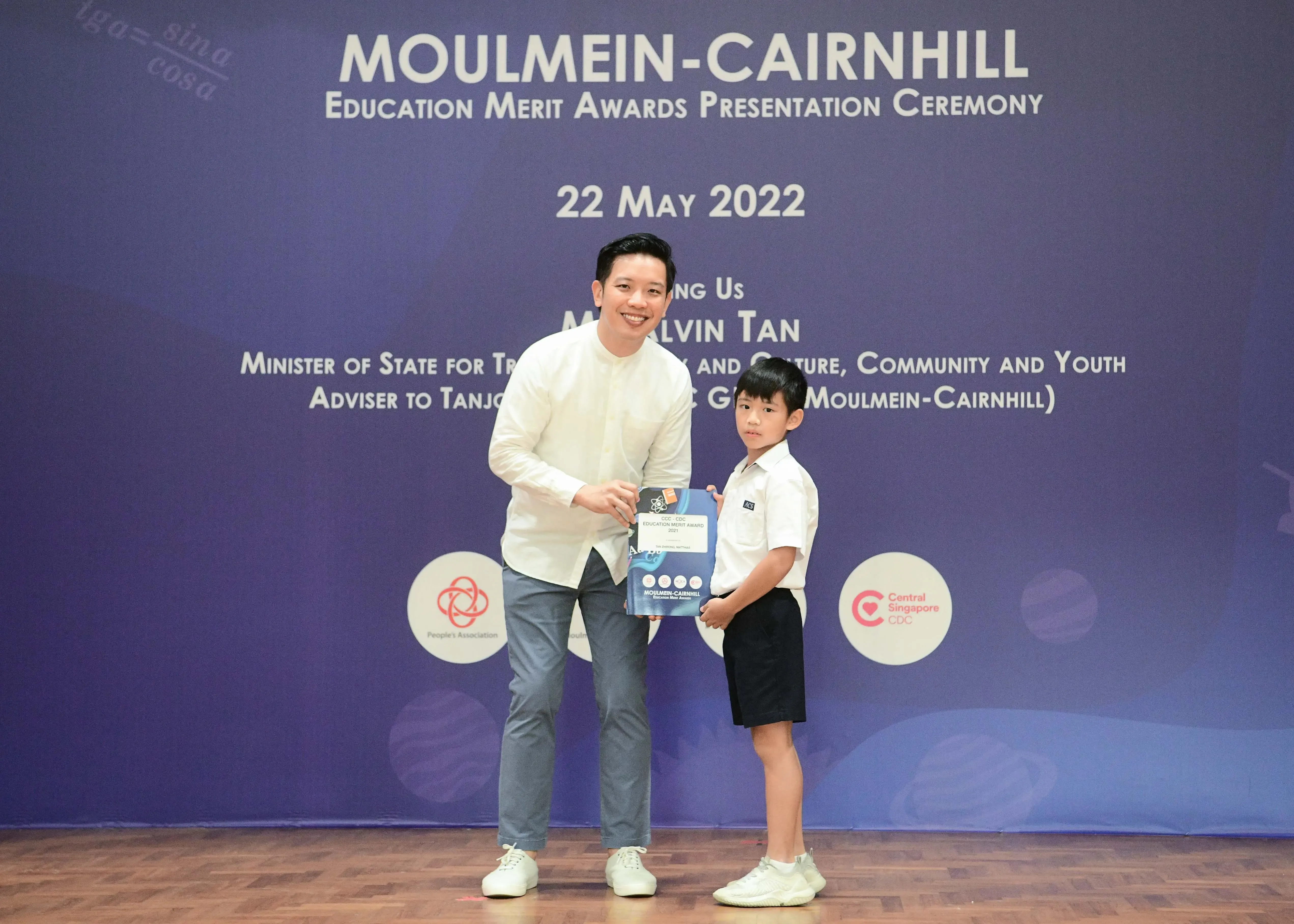 A man and a young boy hold an award booklet at the Moulmein-Cairnhill Education Merit Awards Ceremony on 22 May 2022.