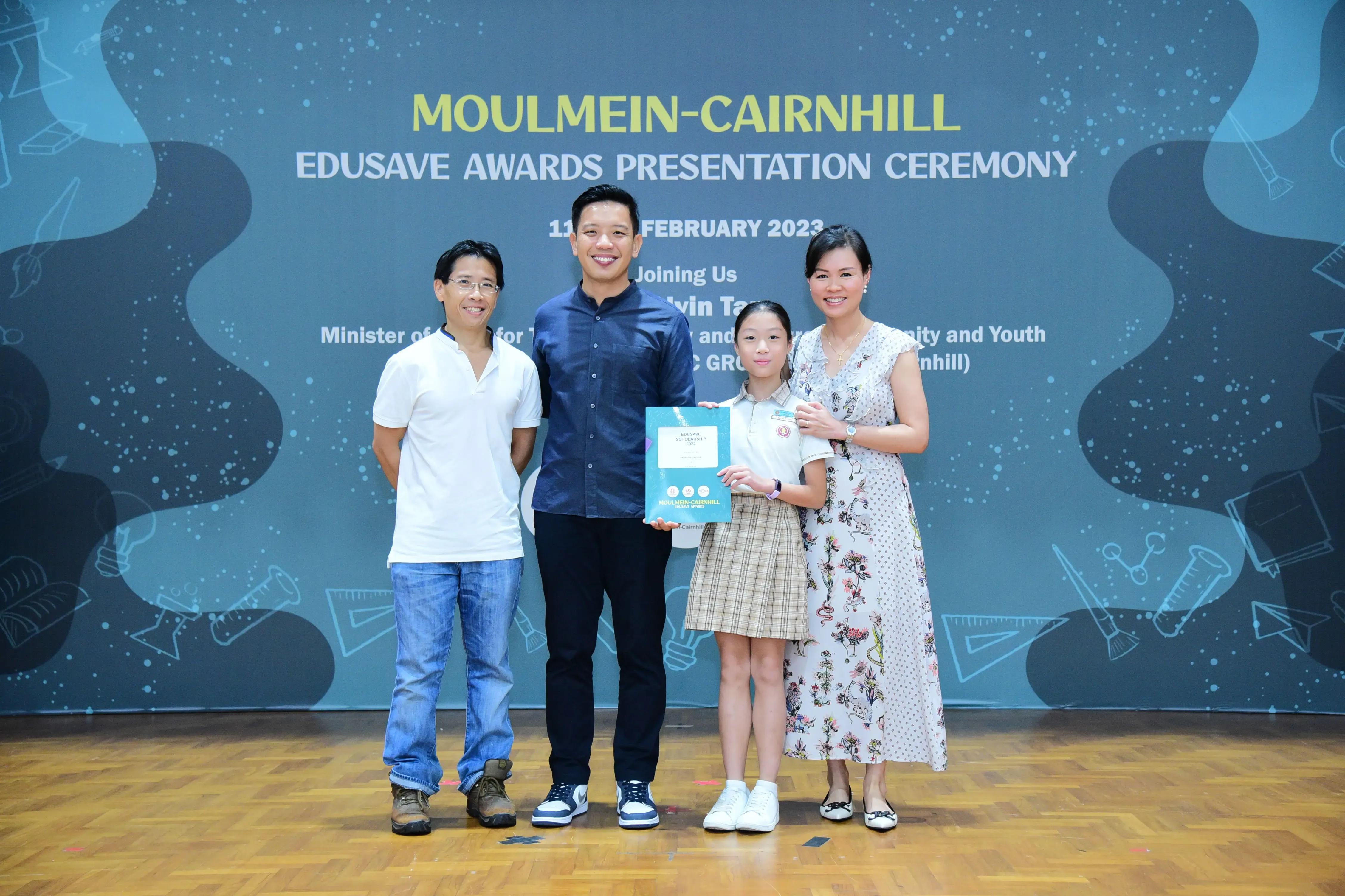 Four people pose on a stage at the Moulmein-Cairnhill Edusave Awards Presentation Ceremony, February 2023.