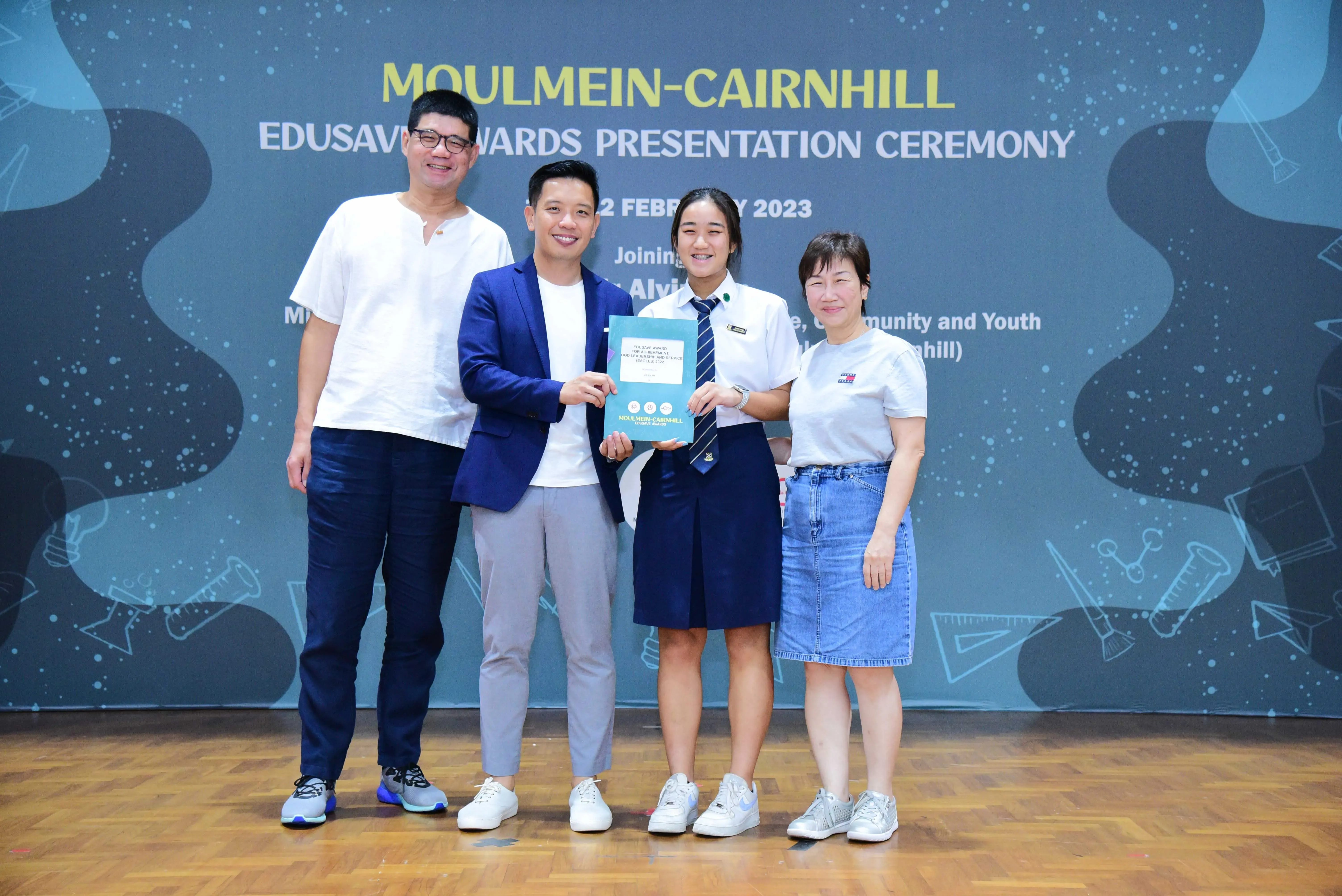 Four people pose on a stage at the Moulmein-Cairnhill Edusave Awards Presentation Ceremony in February 2023.
