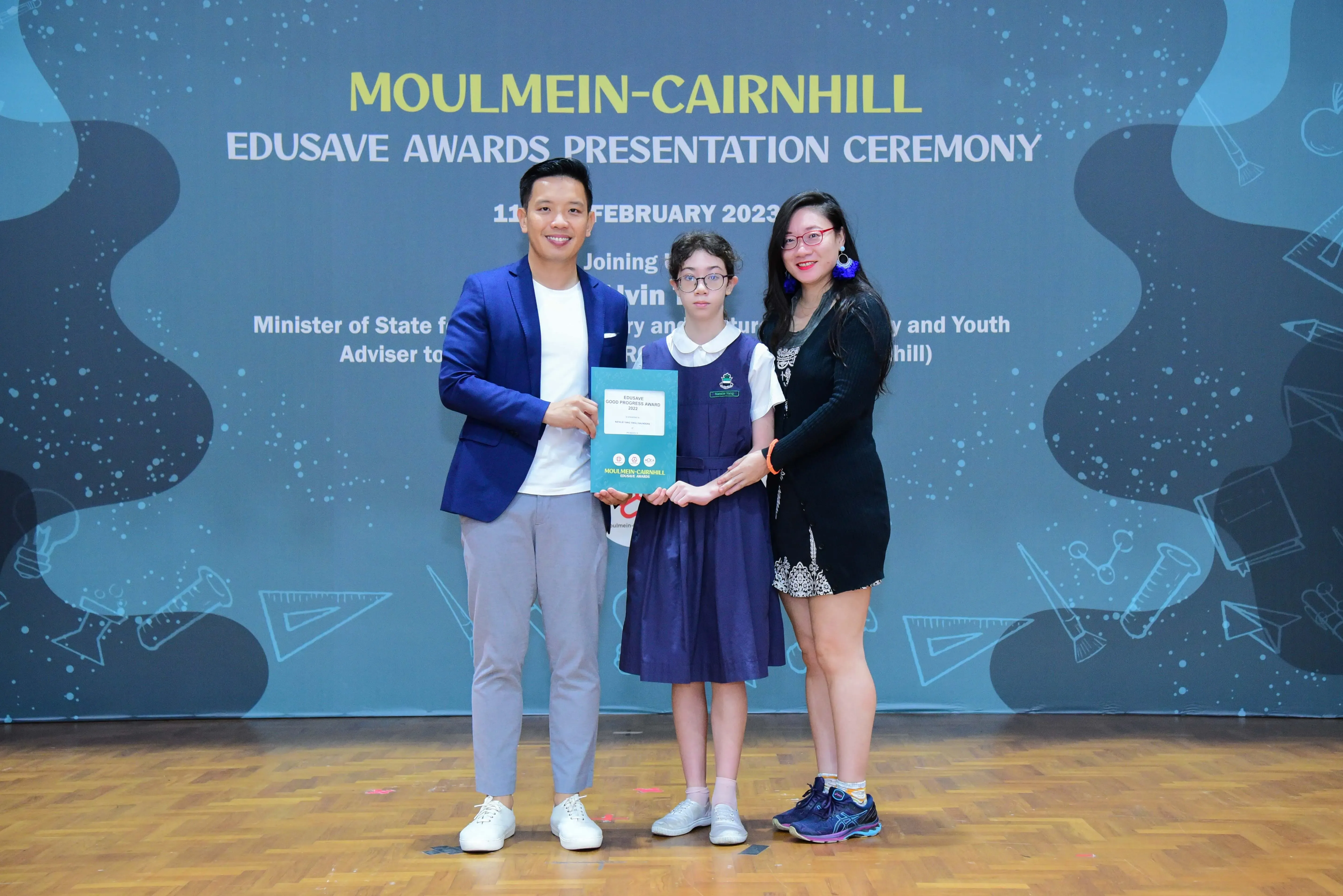 Three people pose holding a certificate at the Moulmein-Cairnhill Edusave Awards Presentation Ceremony in February 2023.