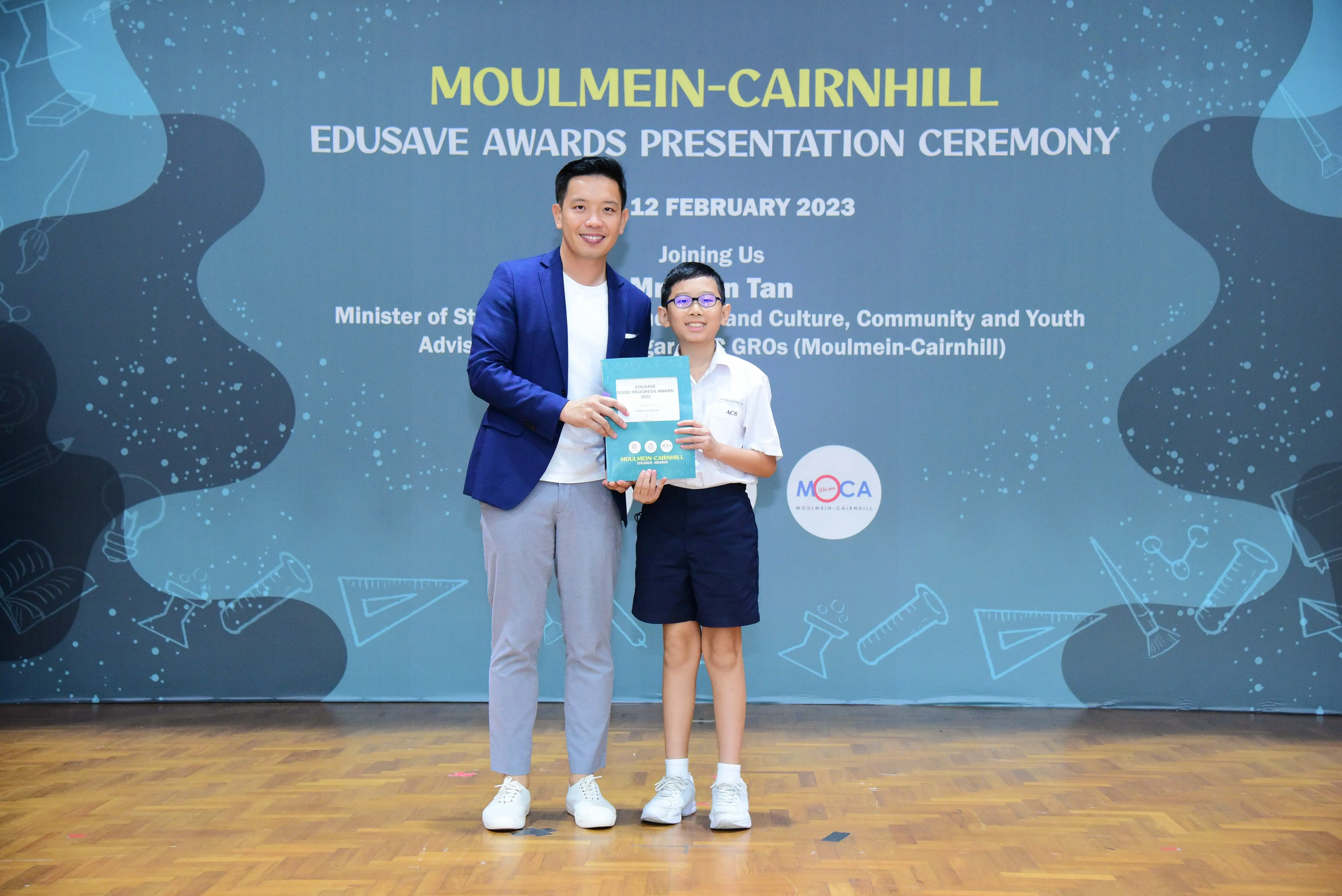 A man in a blue blazer and a young boy in school uniform hold an award at the Moulmein-Cairnhill Edusave Awards Ceremony.