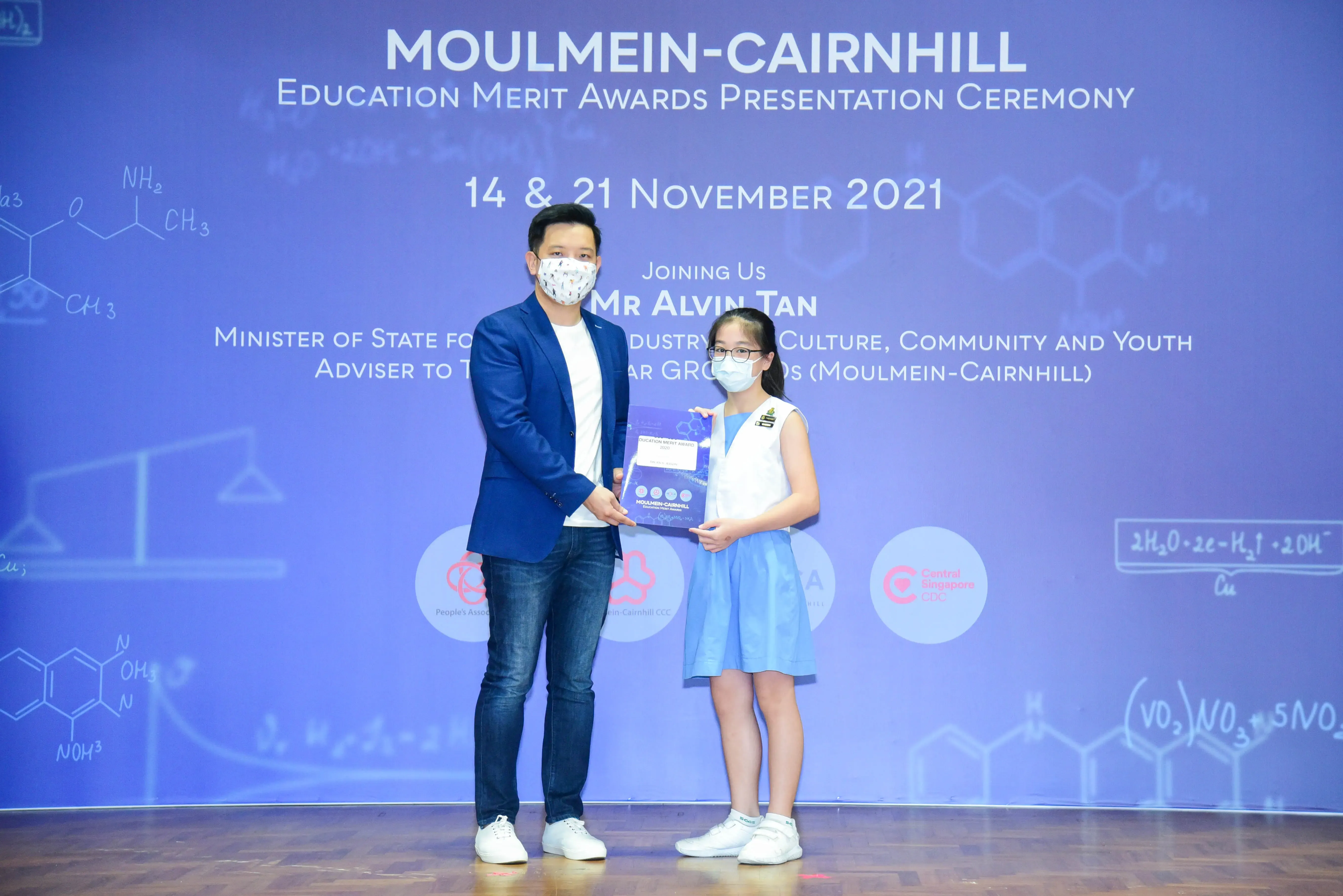 A man and a young girl wearing masks hold an award at the Moulmein-Cairnhill Education Merit Awards ceremony, November 2021.