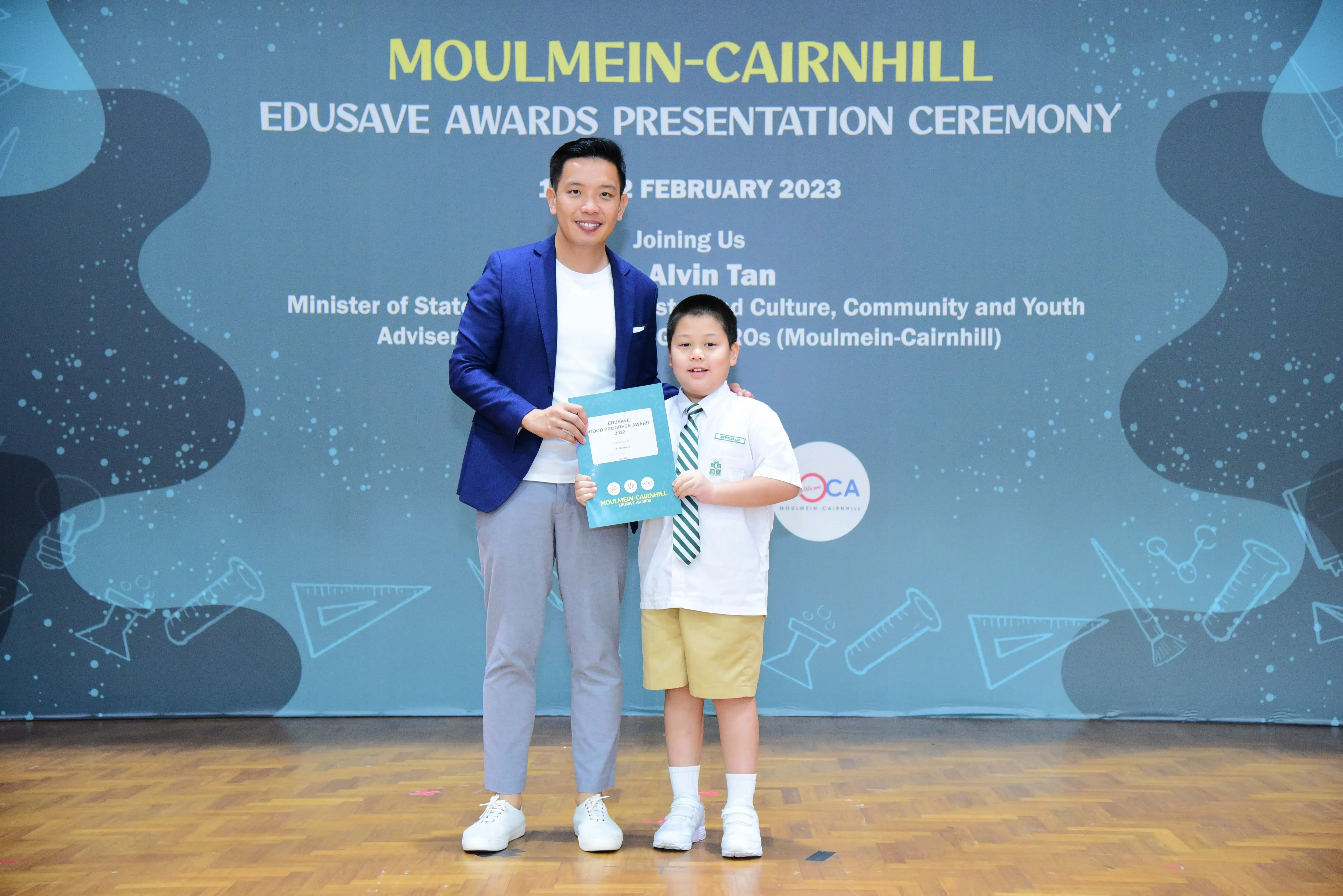 Man in blue blazer and young boy in school uniform hold a certificate at Moulmein-Cairnhill Edusave Awards Ceremony 2023.