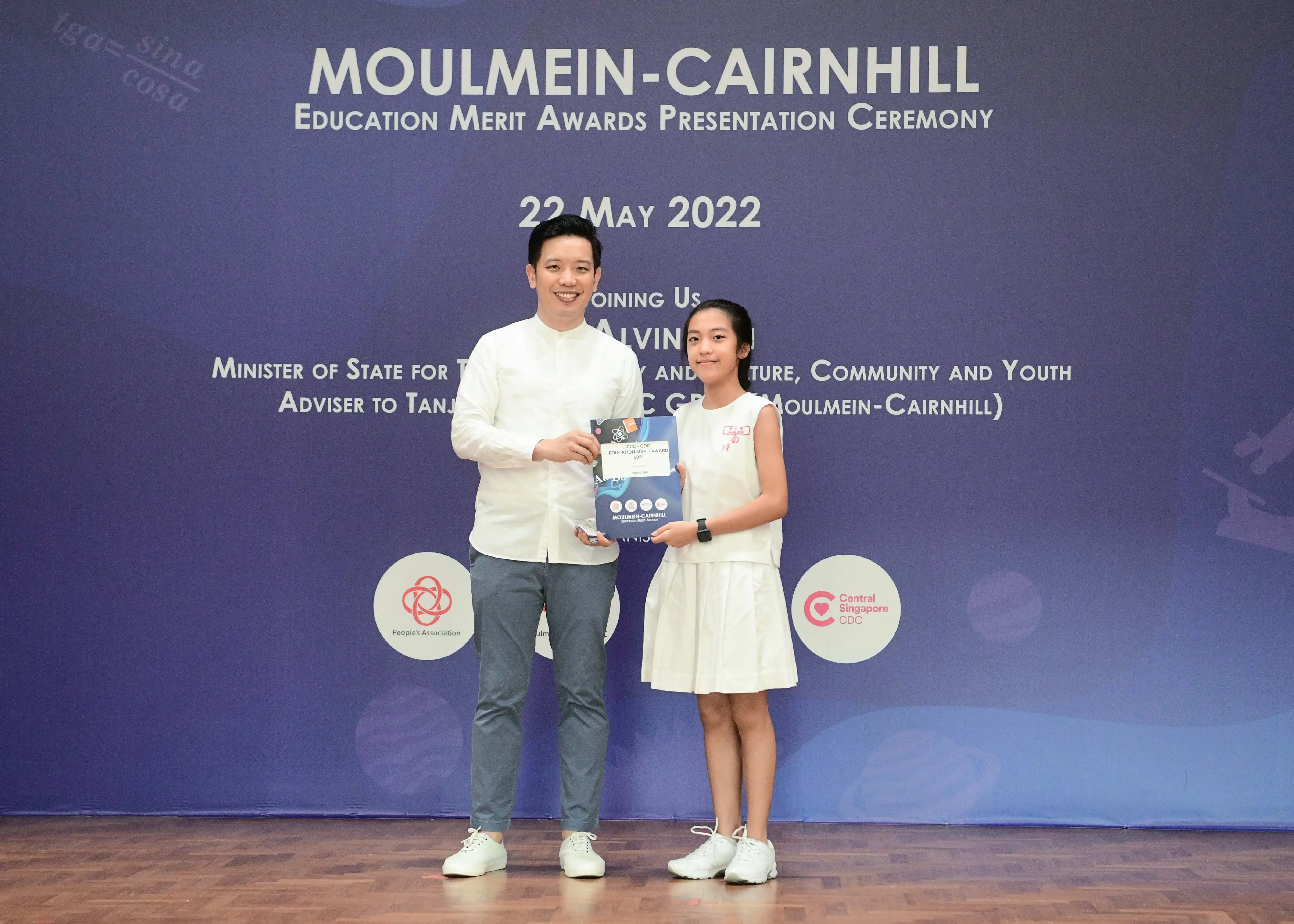 A man and a young girl hold an award certificate at the Moulmein-Cairnhill Education Merit Awards Ceremony on 22 May 2022.