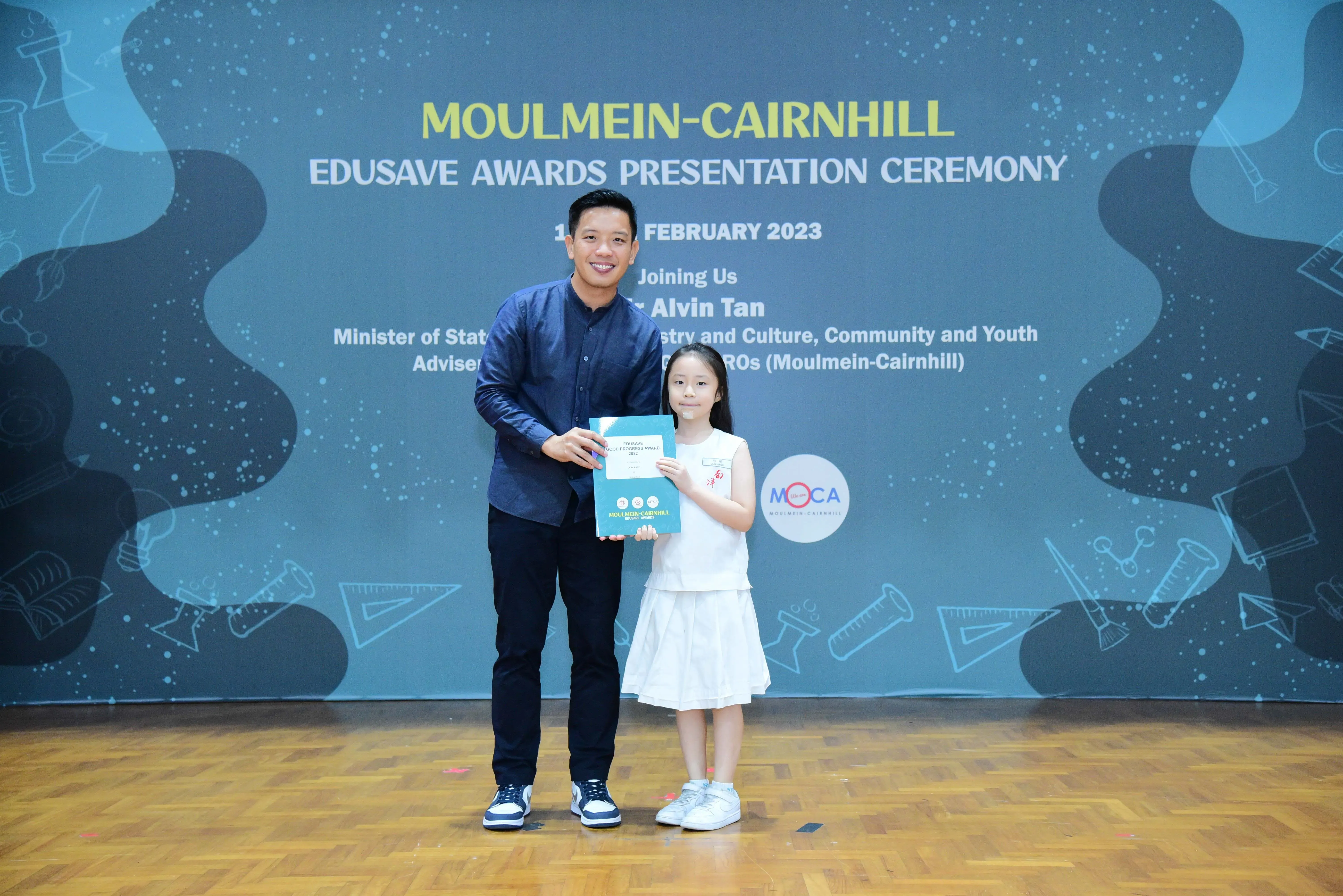 A man and a young girl hold a certificate together at the Moulmein-Cairnhill Edusave Awards Presentation Ceremony 2023.