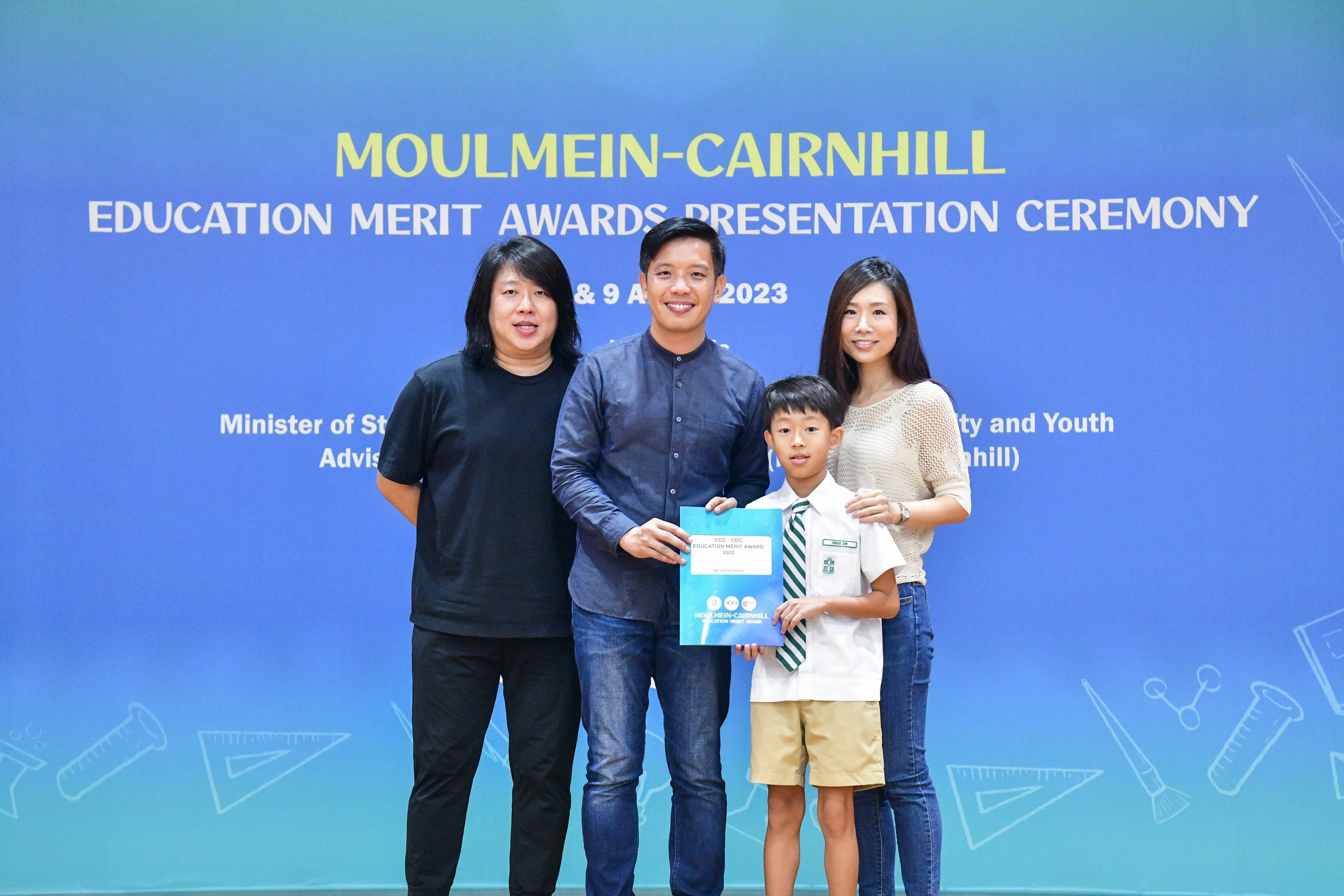 Three adults and a young boy in school uniform hold a certificate at the Moulmein-Cairnhill Education Merit Awards 2023.
