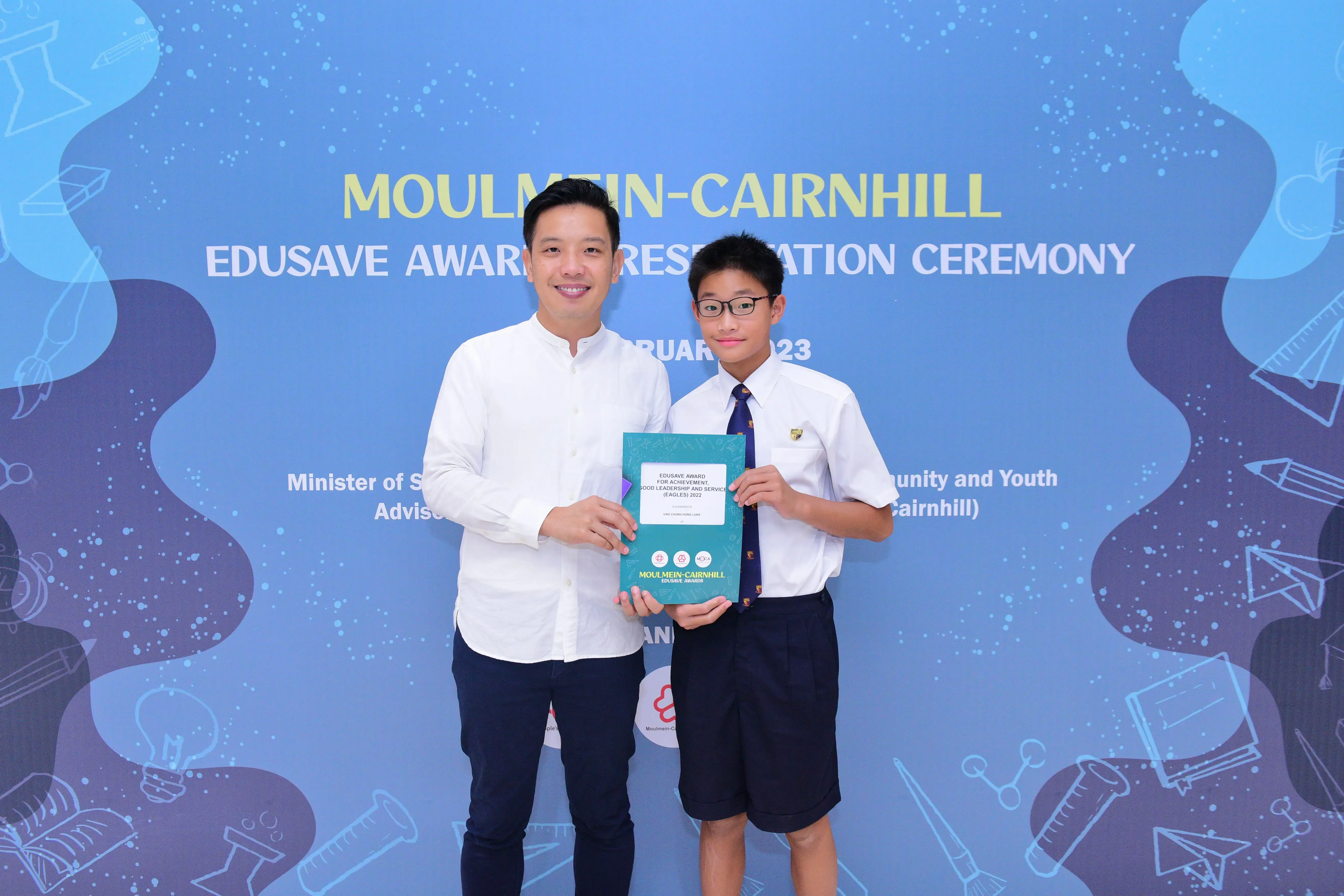 An adult and a uniformed student hold a teal award folder at the Moulmein-Cairnhill Edusave Awards Ceremony 2023.