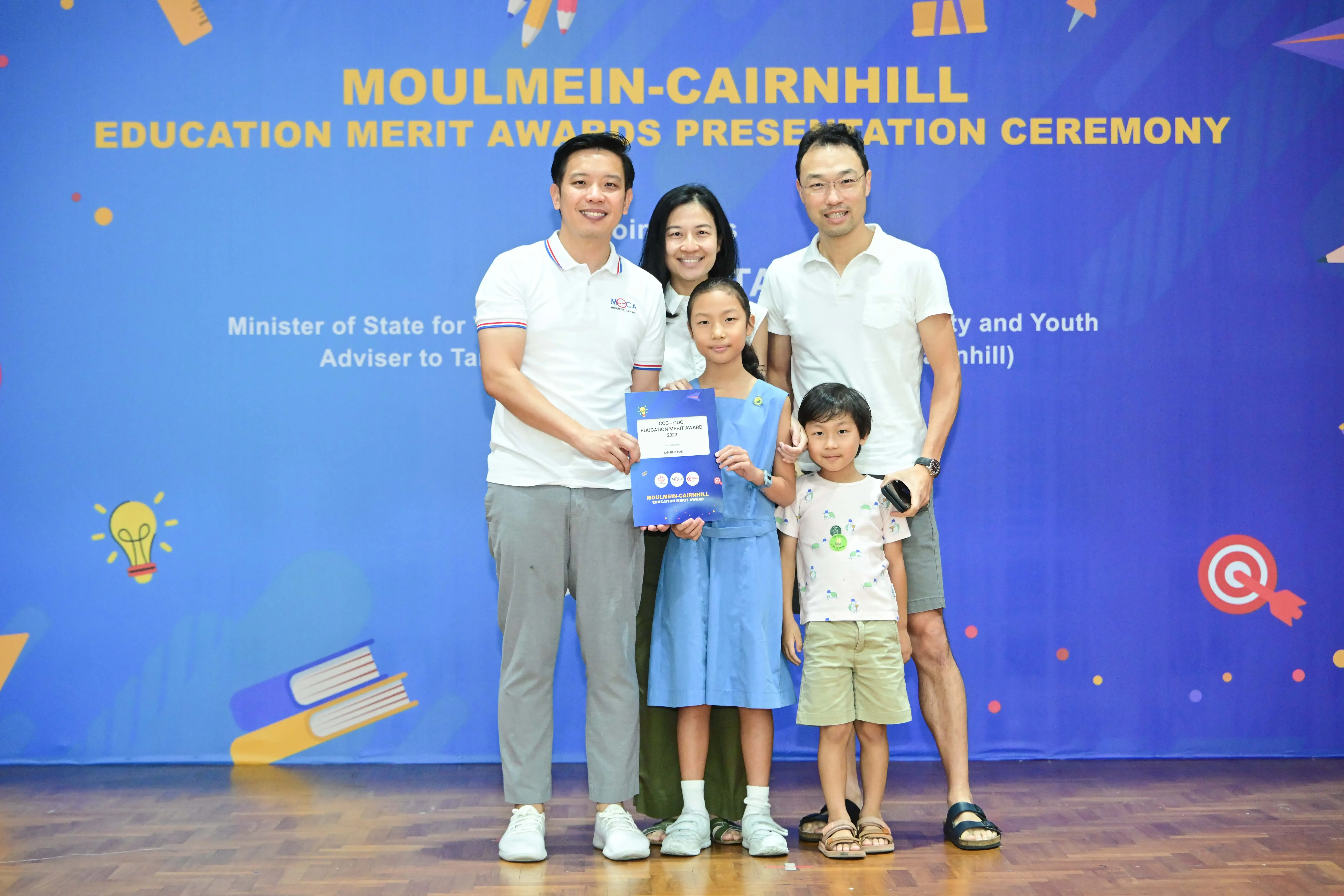 Five people pose at the Moulmein-Cairnhill Education Merit Awards Presentation Ceremony, with a girl holding a certificate.