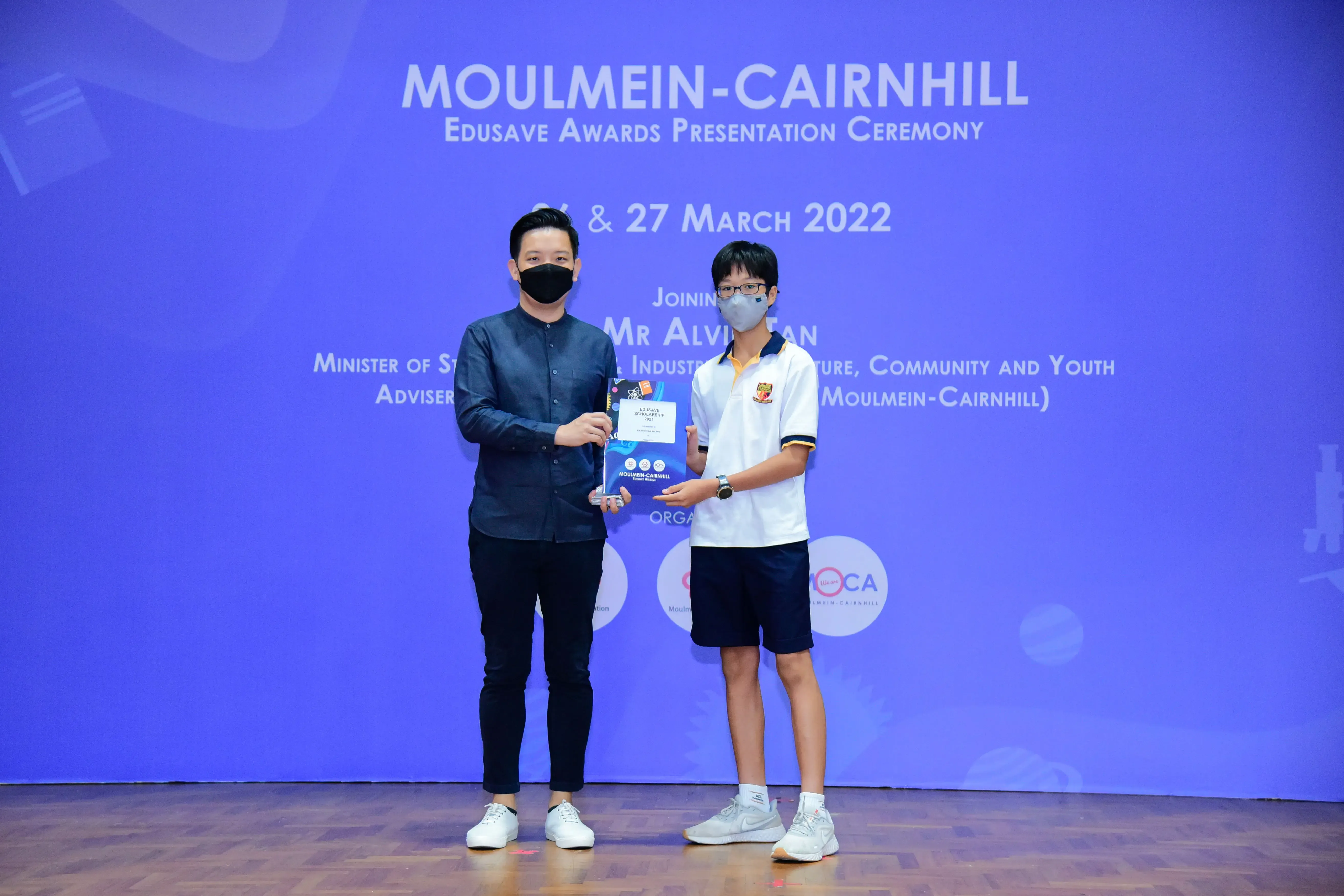 Two masked individuals hold an award at the Moulmein-Cairnhill Edusave Awards Presentation Ceremony, March 2022.