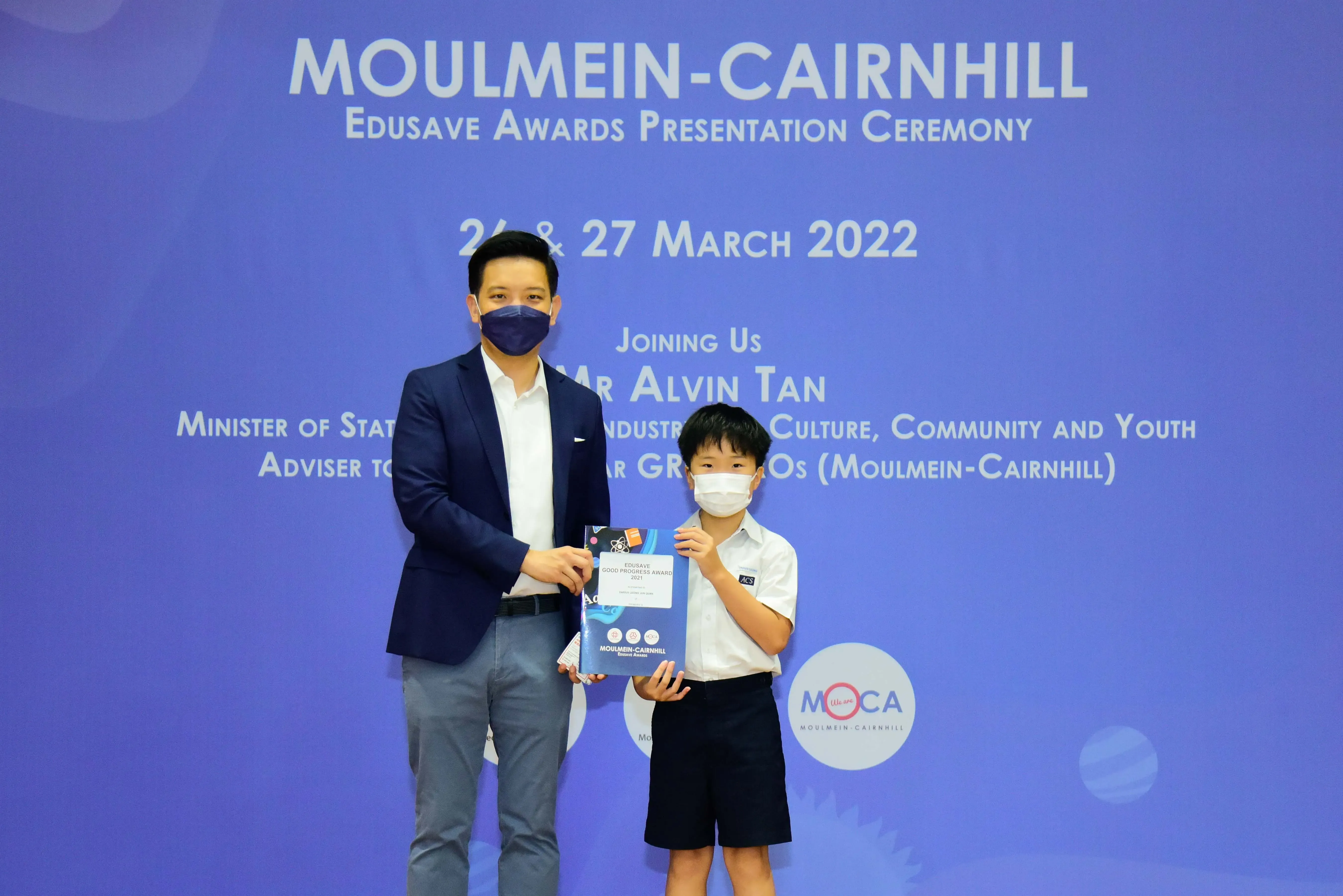 An adult and a young student in masks hold an award at the Moulmein-Cairnhill Edusave Awards Ceremony, March 2022.