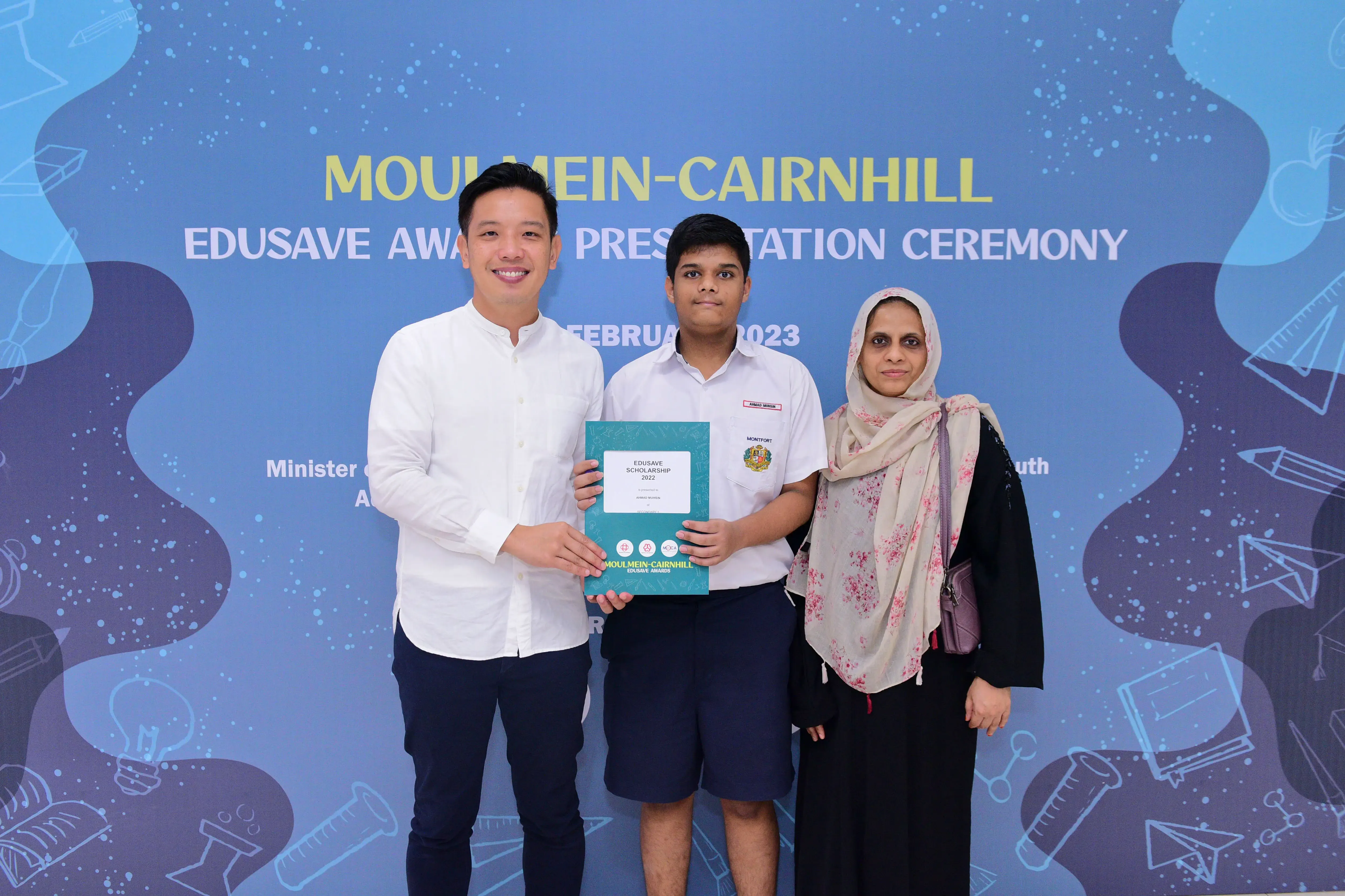 Three people pose holding an Edusave Scholarship certificate at the Moulmein-Cairnhill Edusave Awards Ceremony 2023.