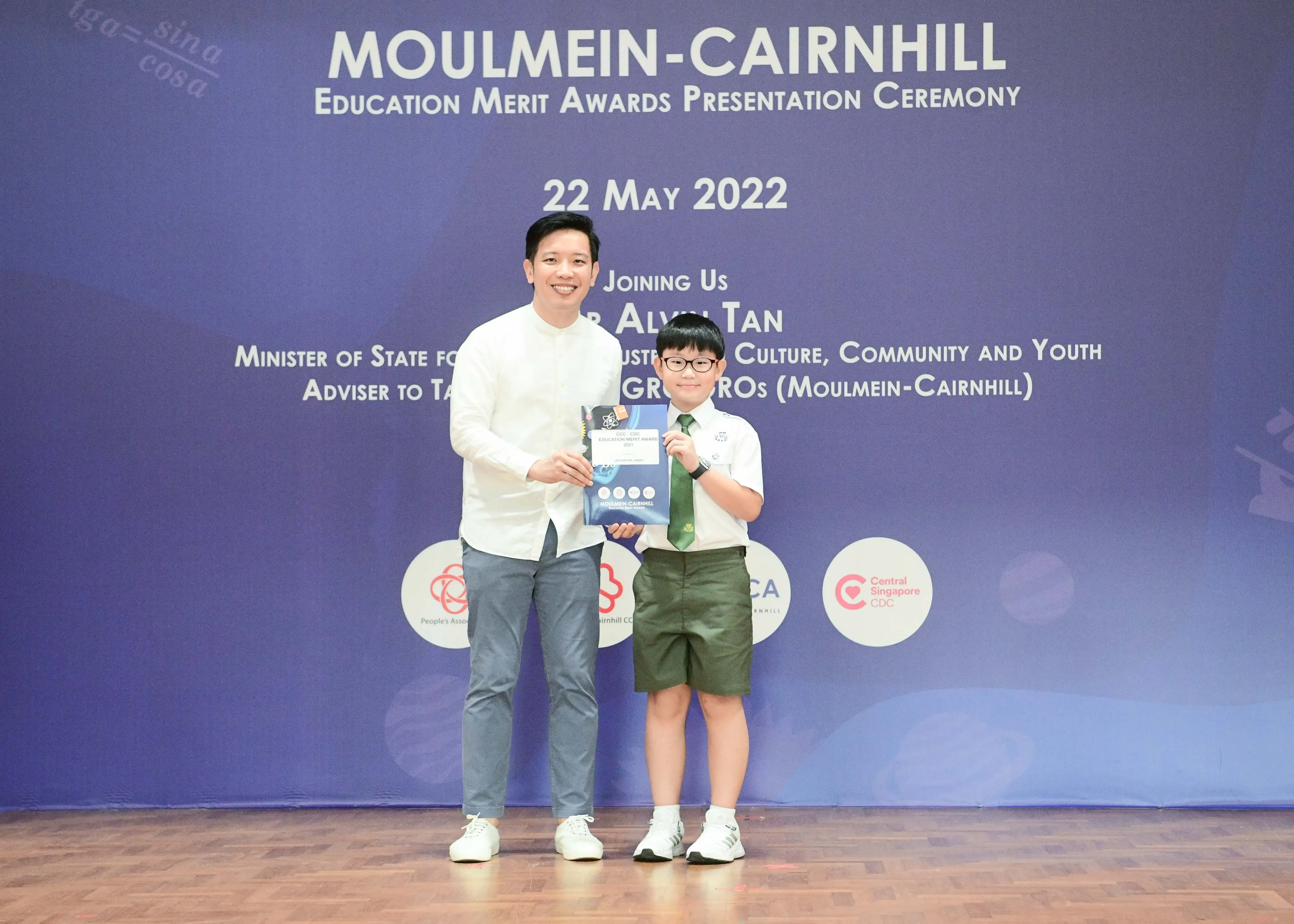Adult and uniformed schoolboy hold an award certificate at Moulmein-Cairnhill Education Merit Awards ceremony on 22 May 2022.