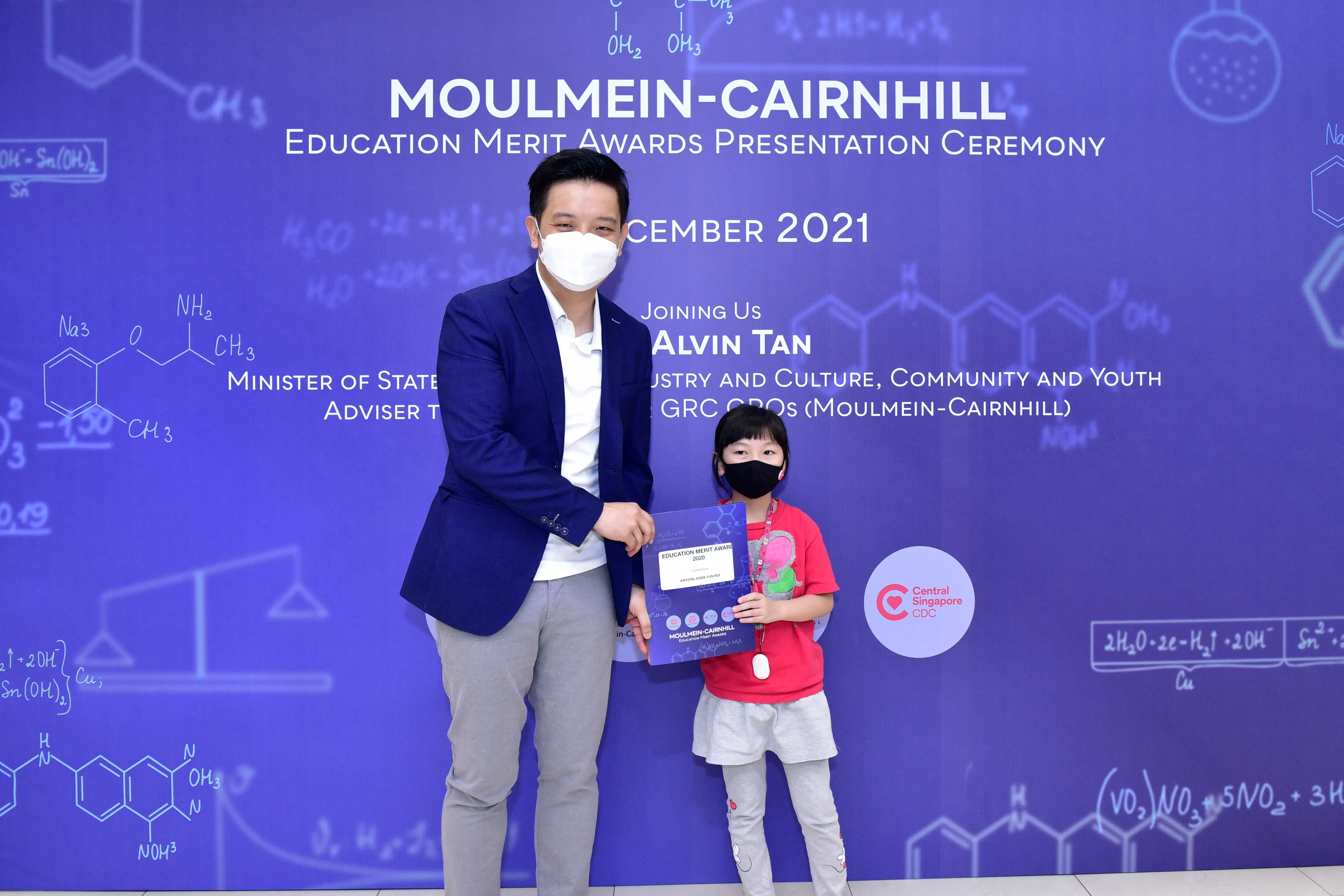 A masked man and young girl hold an award certificate at the Moulmein-Cairnhill Education Merit Awards 2021.