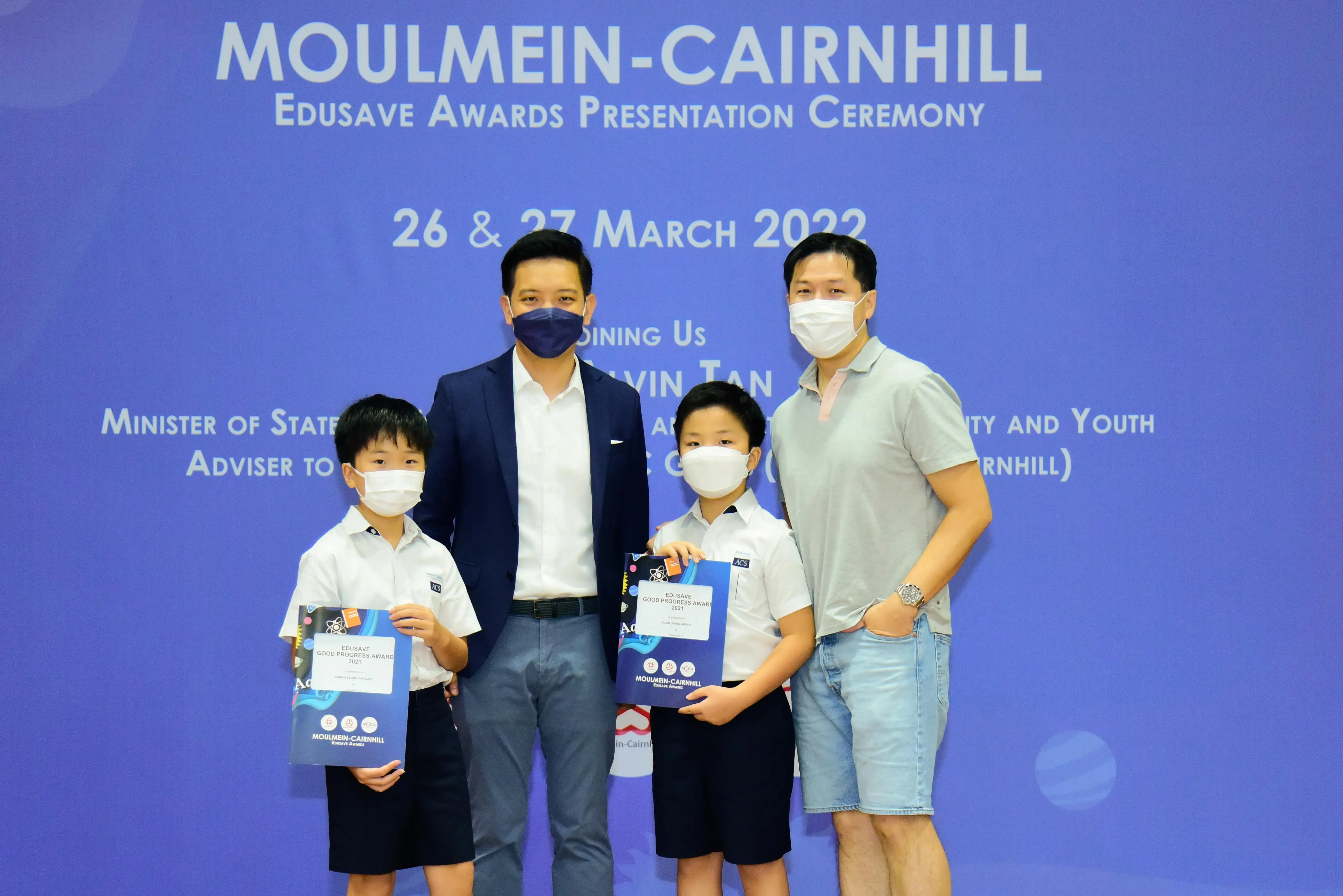 Two masked adults and two young boys holding award folders pose at the Moulmein-Cairnhill Edusave Awards Ceremony 2022.