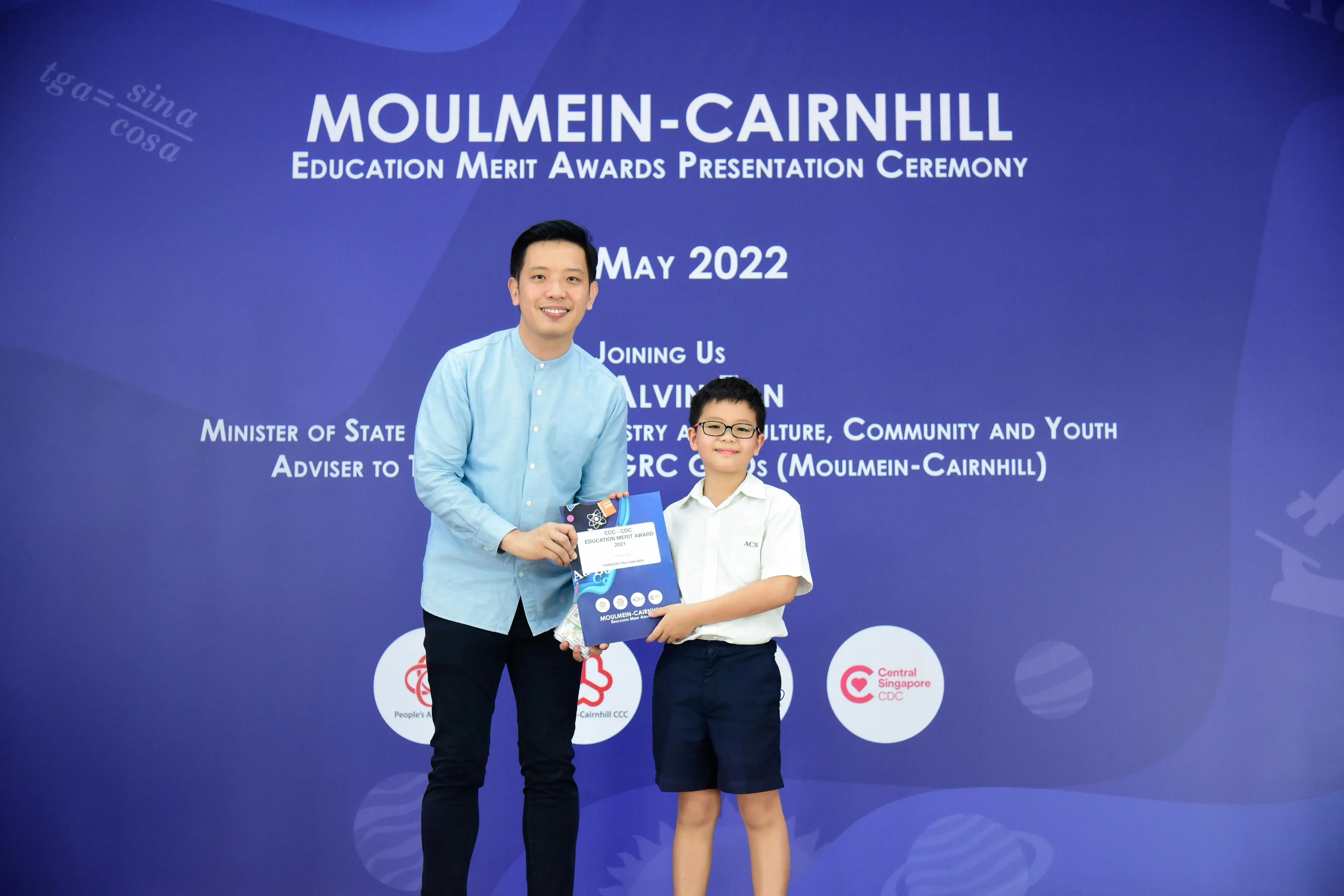 A man and a young boy hold an award certificate at the Moulmein-Cairnhill Education Merit Awards Ceremony, May 2022.