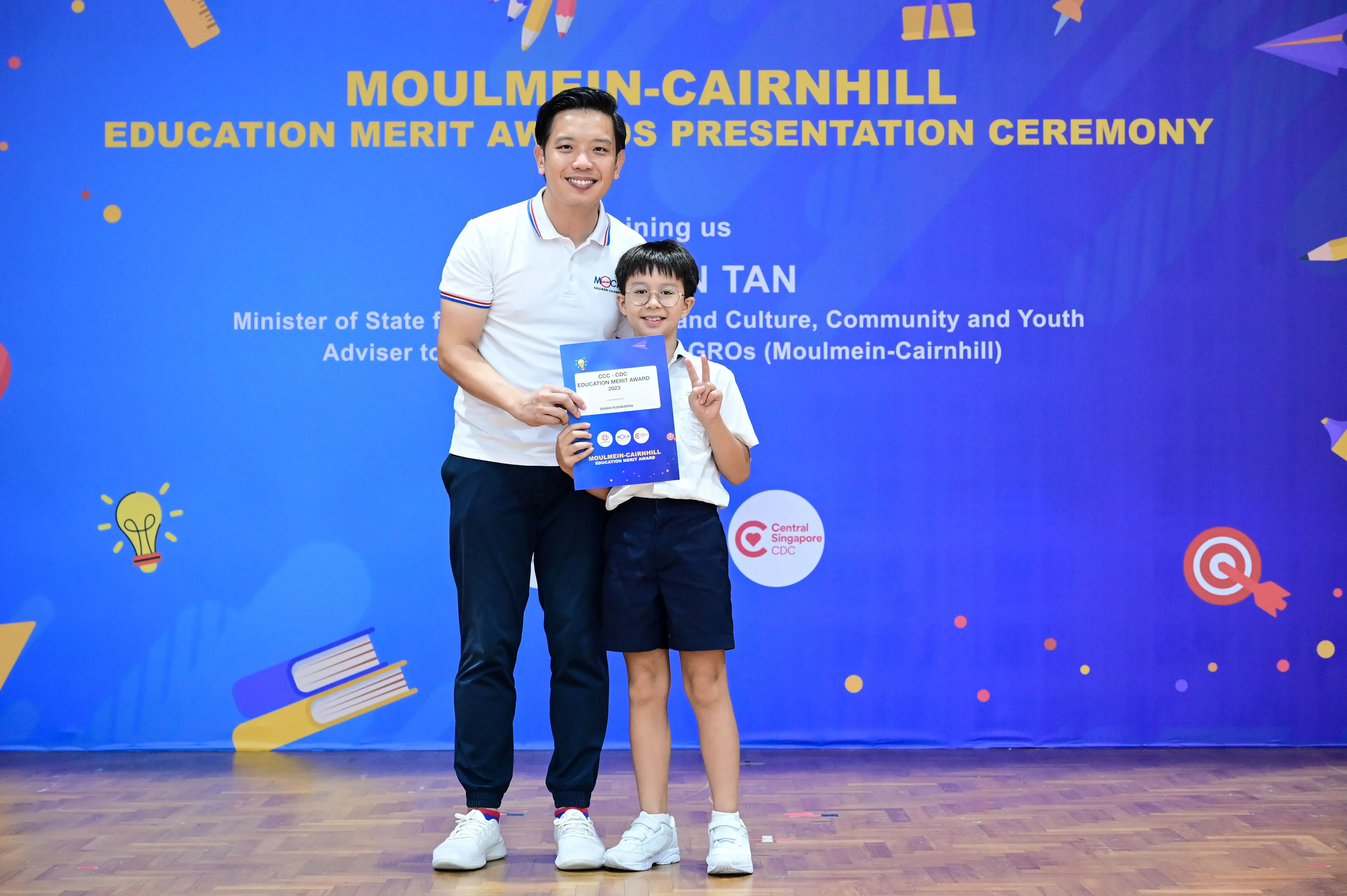 A man and a young boy holding an award certificate at the Moulmein-Cairnhill Education Merit Awards Presentation Ceremony.