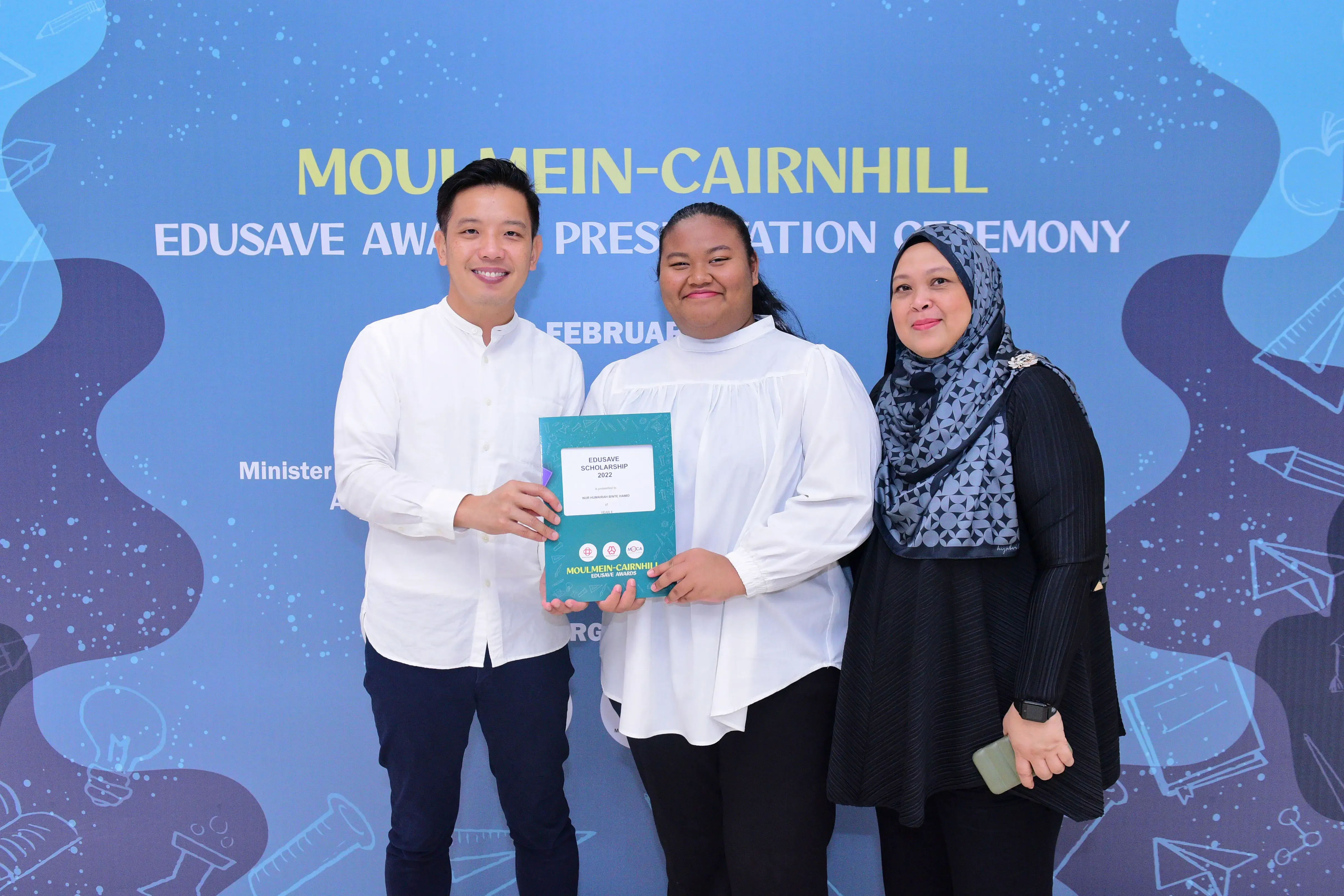 Three people posing at the Moulmein-Cairnhill Edusave Awards Presentation Ceremony, holding a teal scholarship certificate.