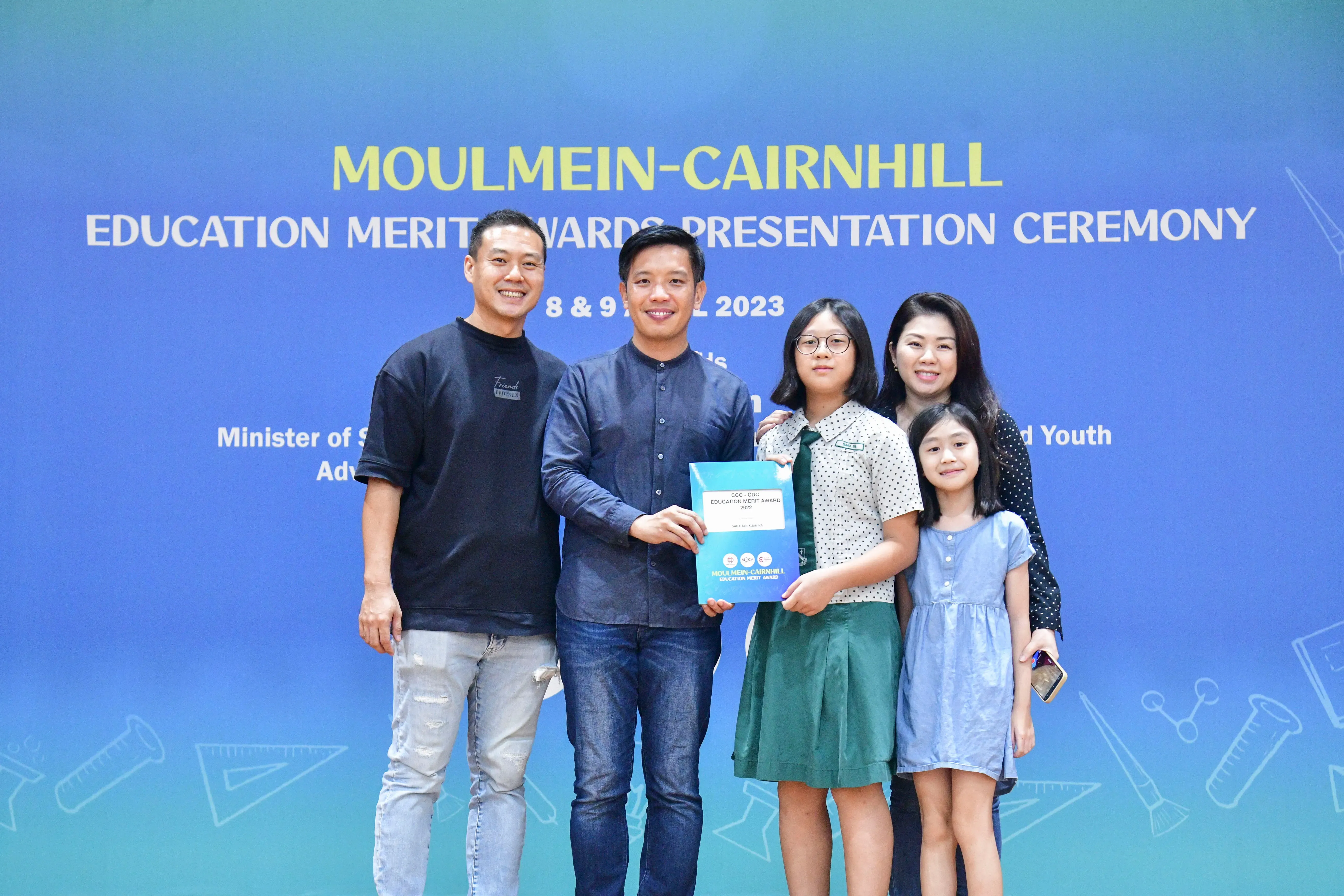 Five people pose at the Moulmein-Cairnhill Education Merit Awards Presentation Ceremony 2023, holding a blue award folder.