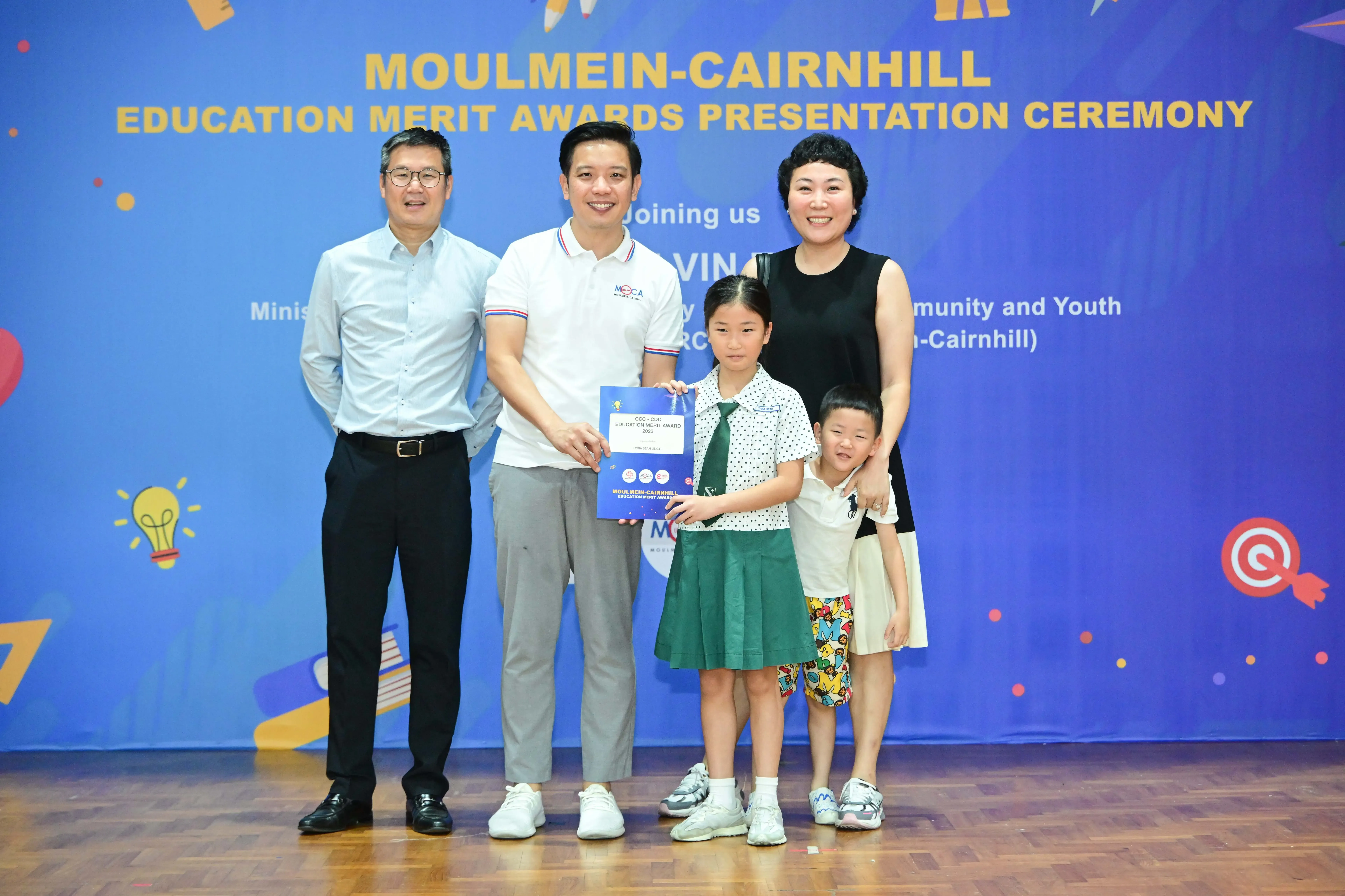 Three adults and two children pose with an award certificate at the Moulmein-Cairnhill Education Merit Awards Presentation Ceremony.