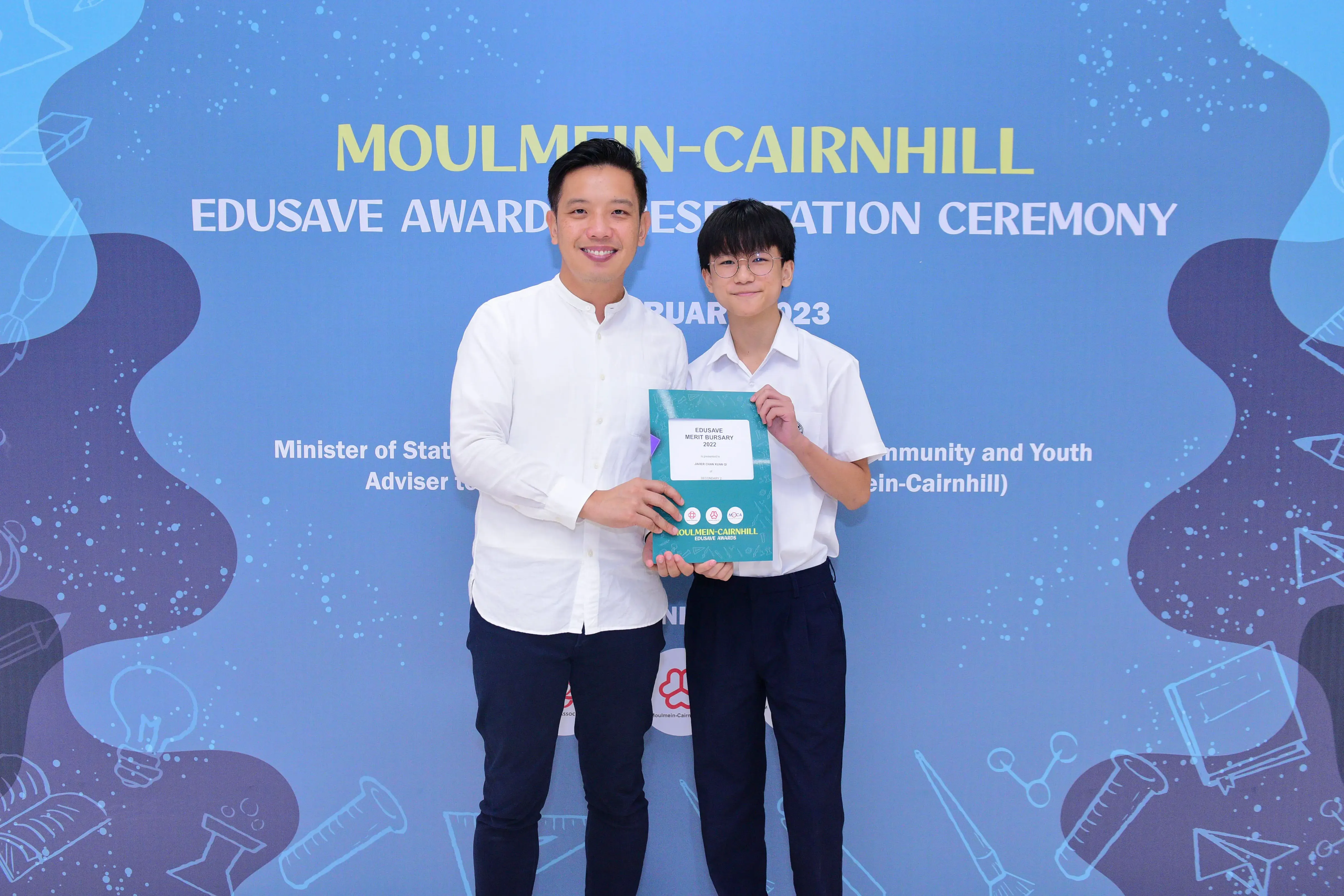 Two people hold an Edusave Merit Bursary booklet at the Moulmein-Cairnhill Edusave Awards Presentation Ceremony 2023.