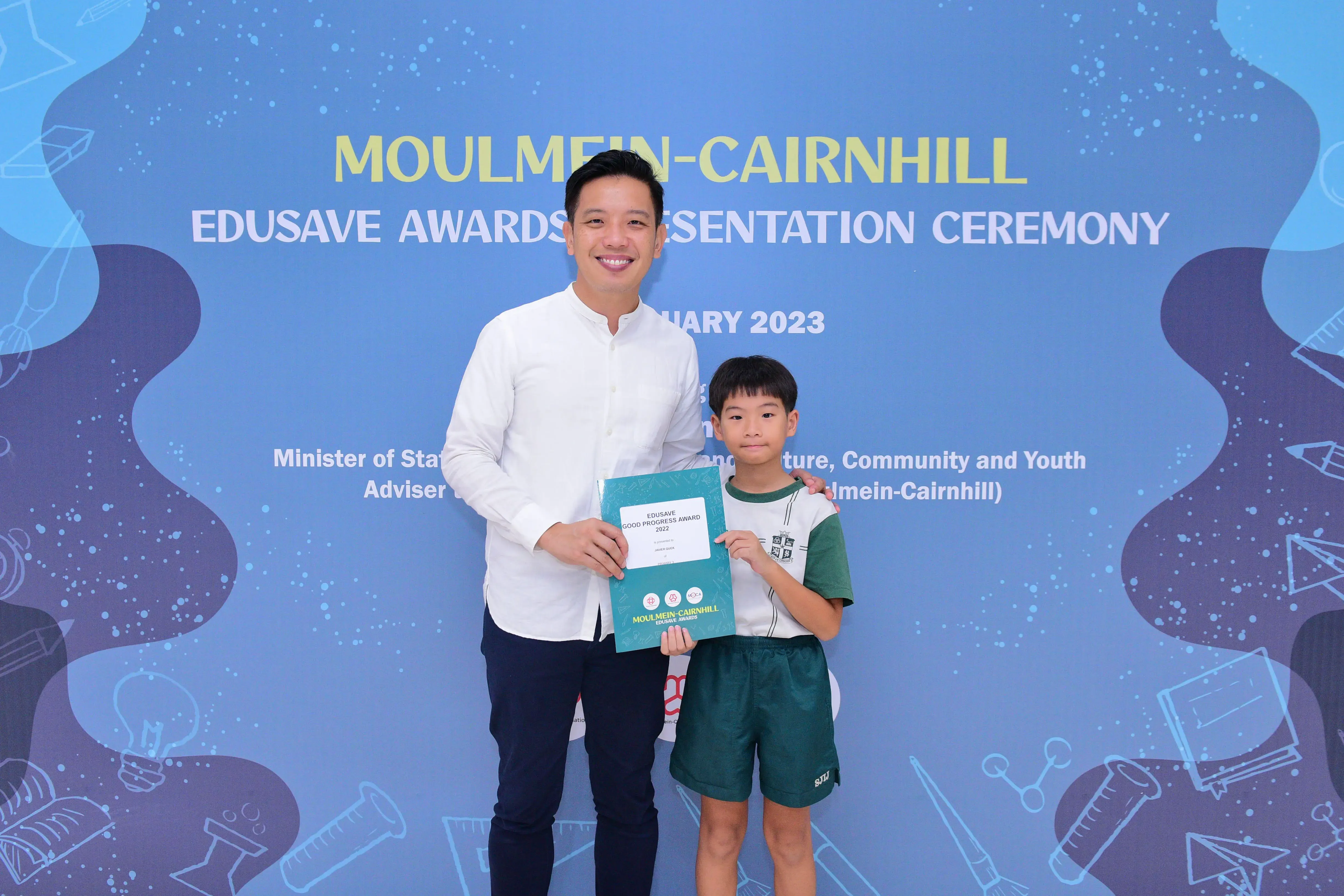 A man and a young boy pose together holding an Edusave Good Progress Award at the Moulmein-Cairnhill ceremony 2023.