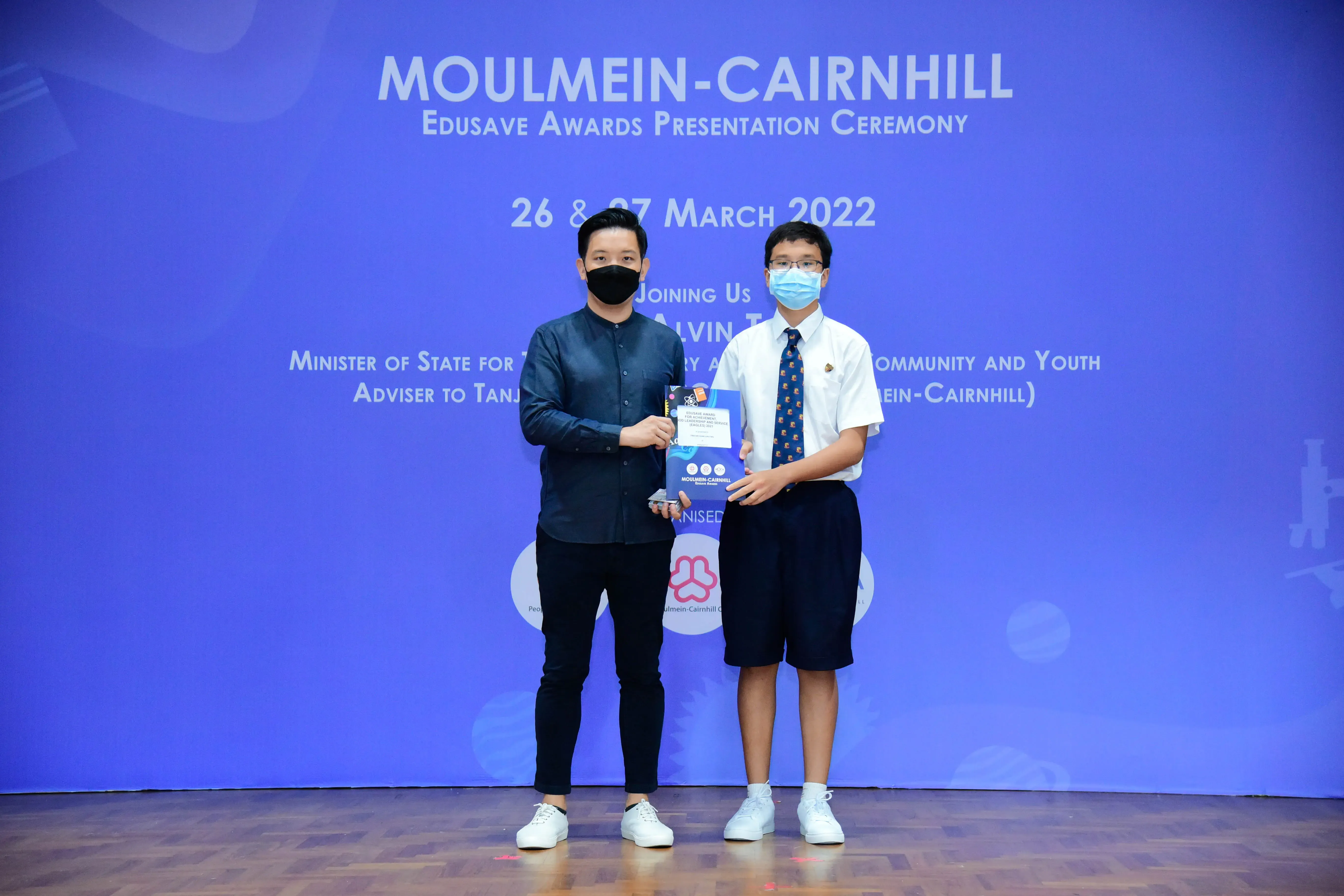 Two masked individuals hold an award at the Moulmein-Cairnhill Edusave Awards Ceremony on 26-27 March 2022.