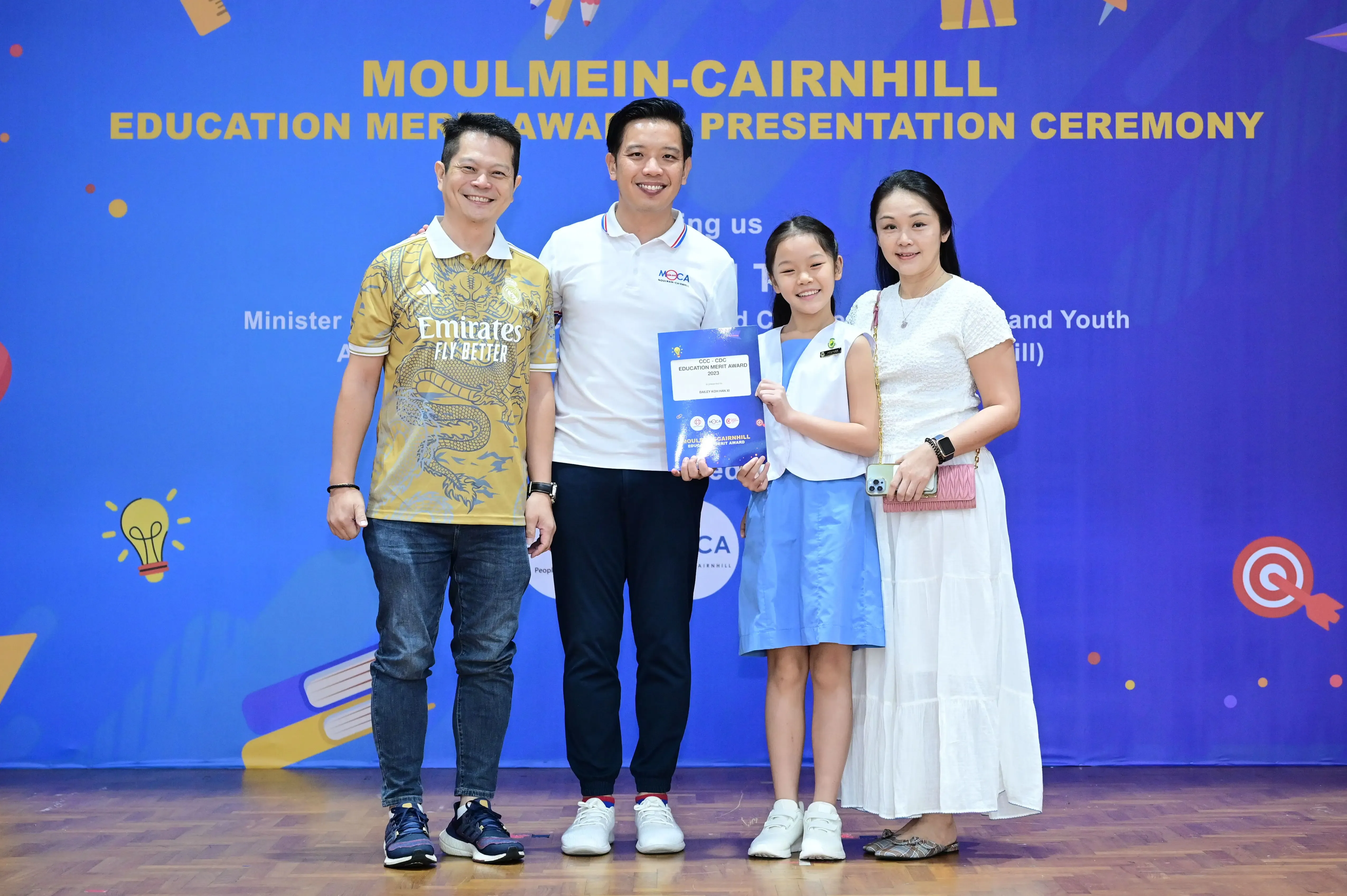 Four people pose at the Moulmein-Cairnhill Education Merit Award Presentation Ceremony, with a girl holding an award certificate.