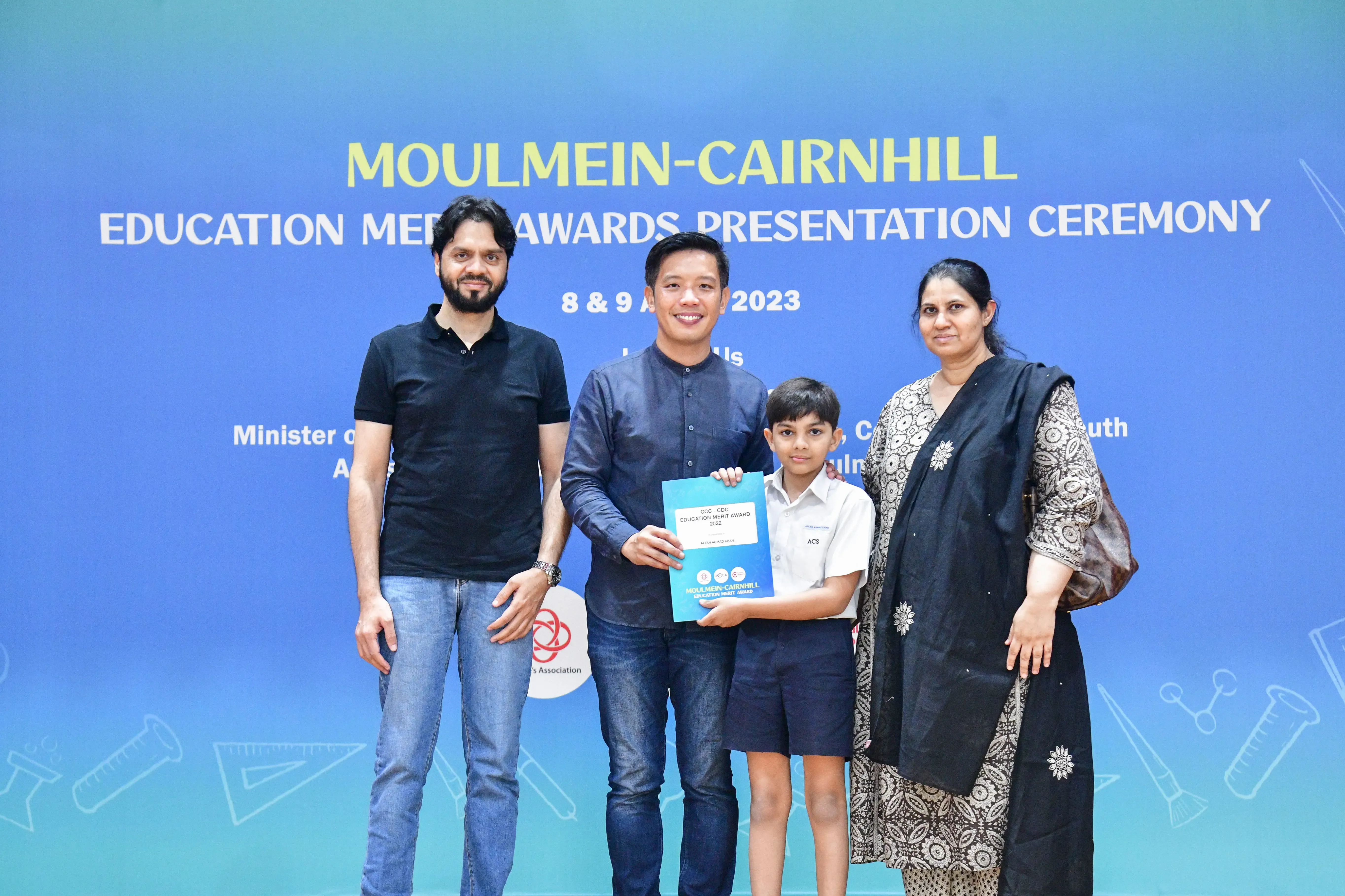 Four people pose at the Moulmein-Cairnhill Education Merit Awards Presentation Ceremony 2023, with a child holding an award.