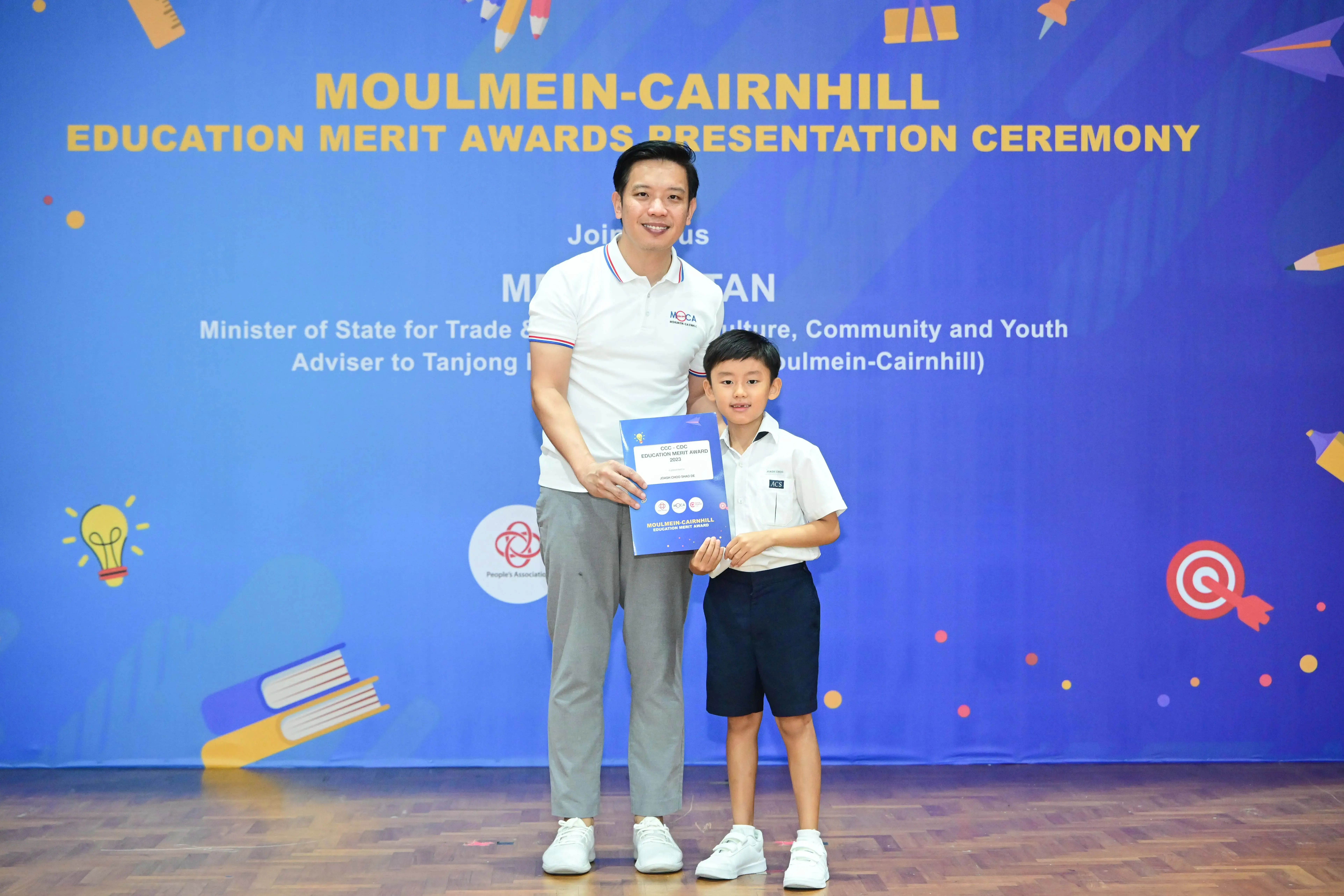 A man and a young boy hold a certificate together at the Moulmein-Cairnhill Education Merit Awards ceremony.