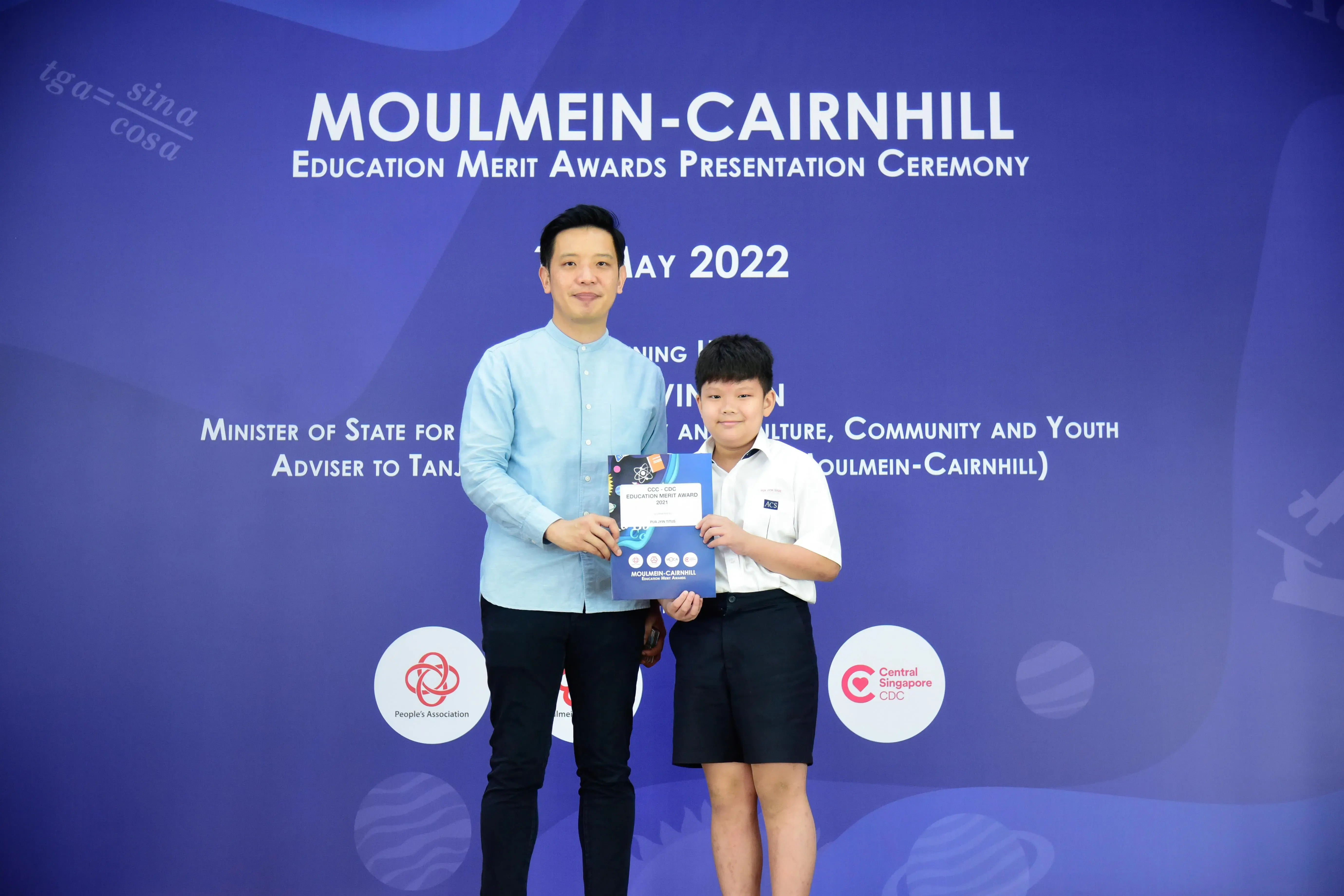 An adult and a young student pose holding an award at the Moulmein-Cairnhill Education Merit Awards Ceremony, May 2022.