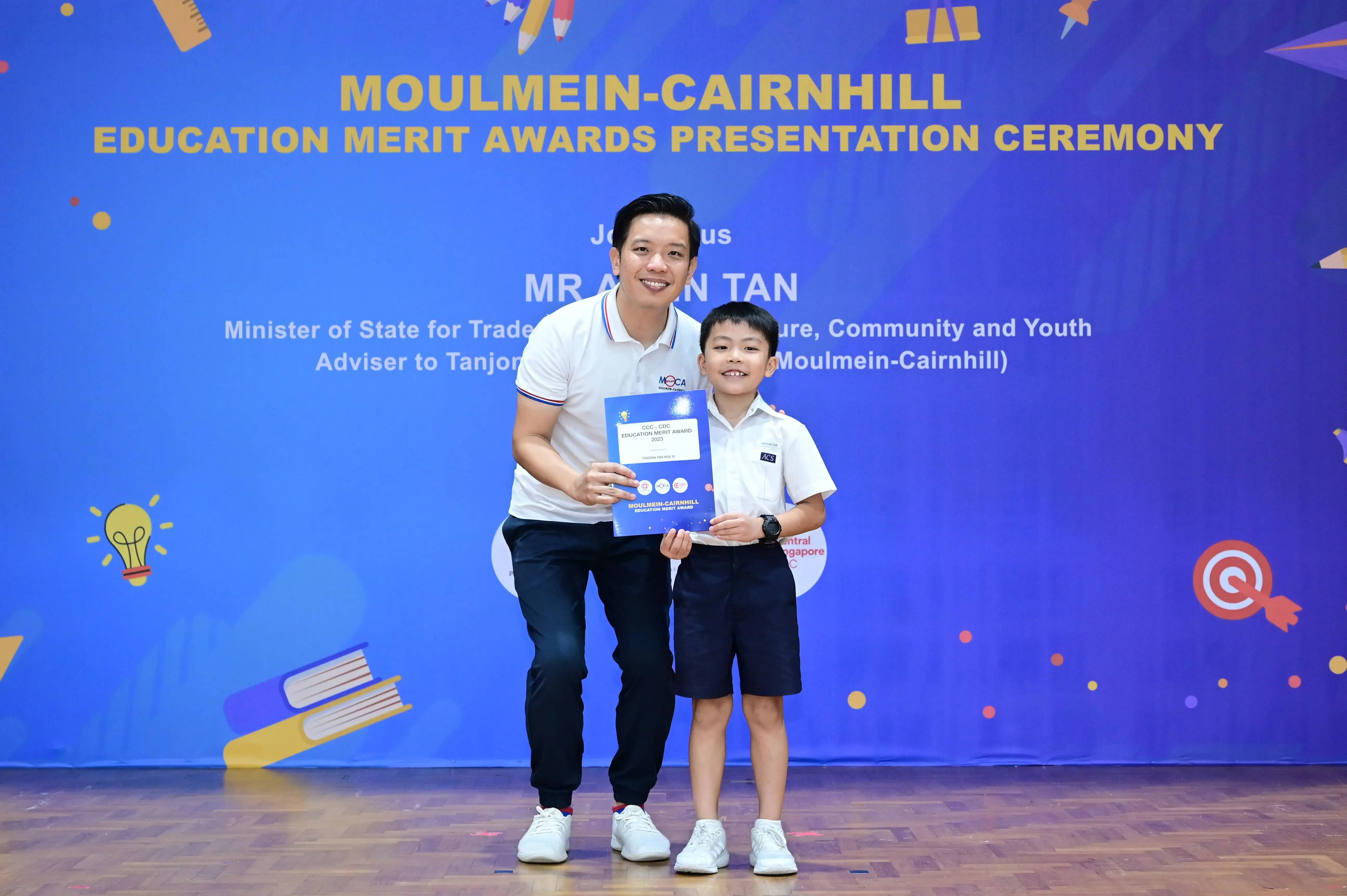 Man and young boy pose holding an award certificate at Moulmein-Cairnhill Education Merit Awards ceremony.