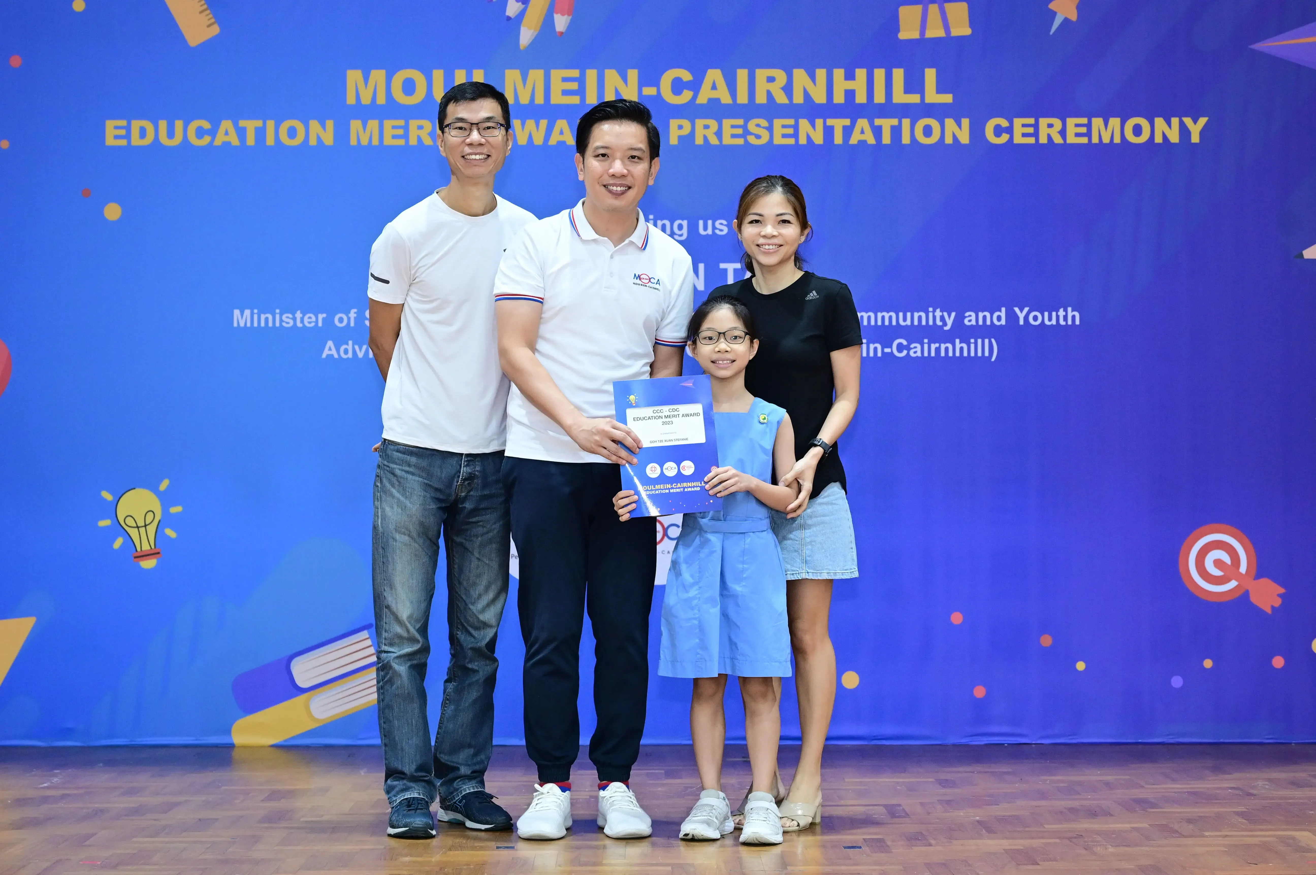 Three adults and a young girl holding a certificate pose at the Moulmein-Cairnhill Education Merit Award Ceremony.