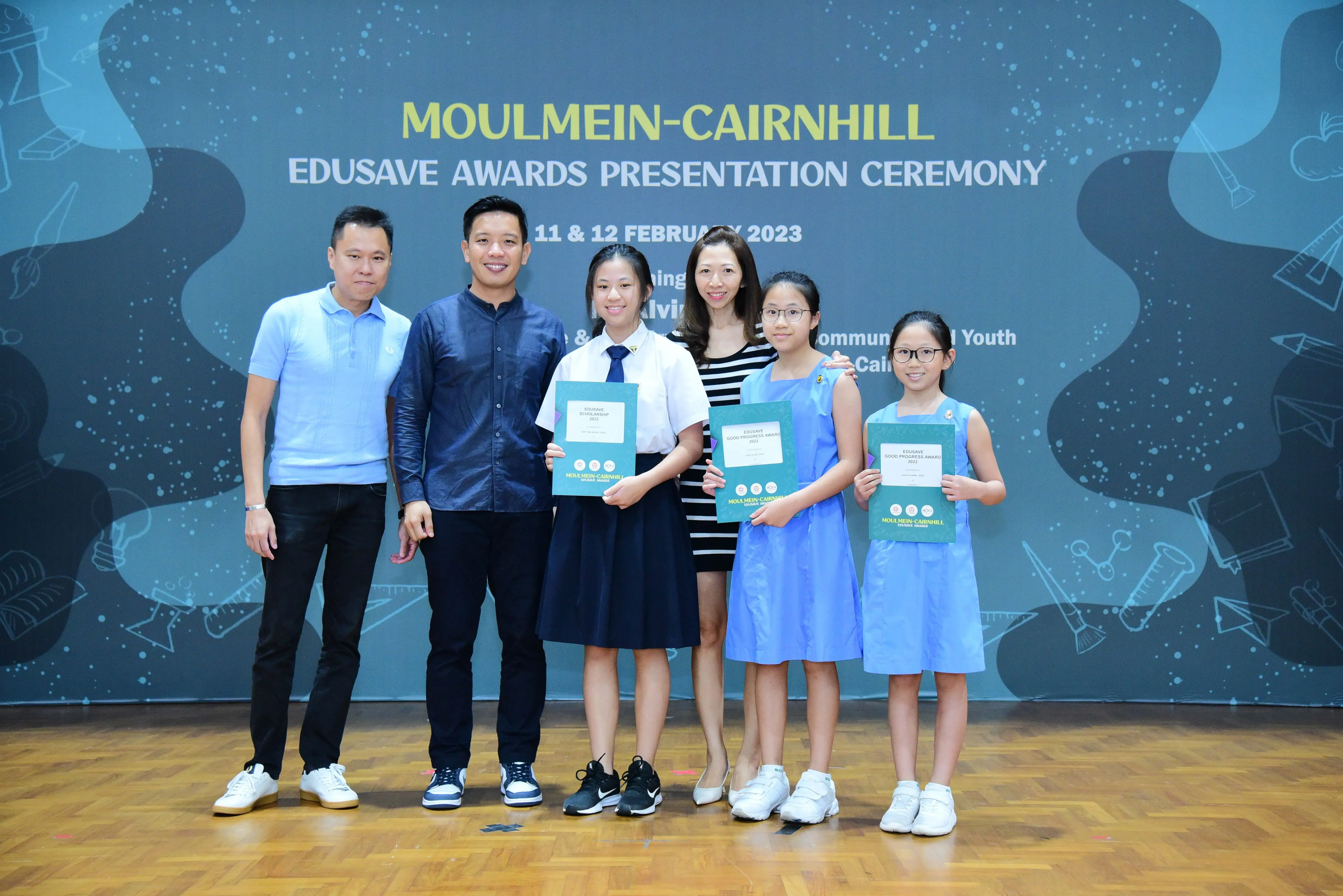 Six people pose at the Moulmein-Cairnhill Edusave Awards Presentation Ceremony, with three girls holding teal certificates.