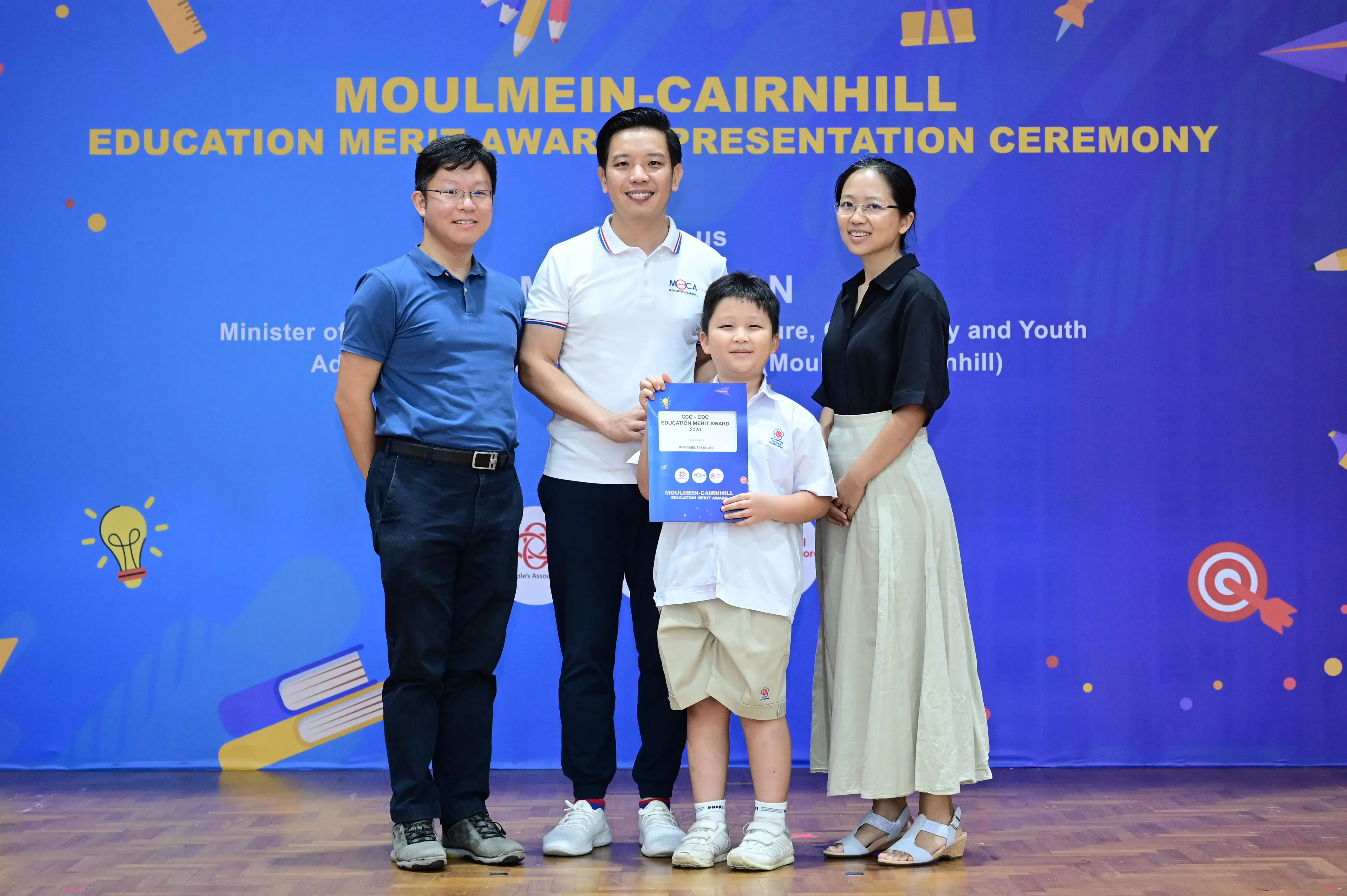 Three adults and a boy holding an award certificate pose at the Moulmein-Cairnhill Education Merit Award Ceremony.