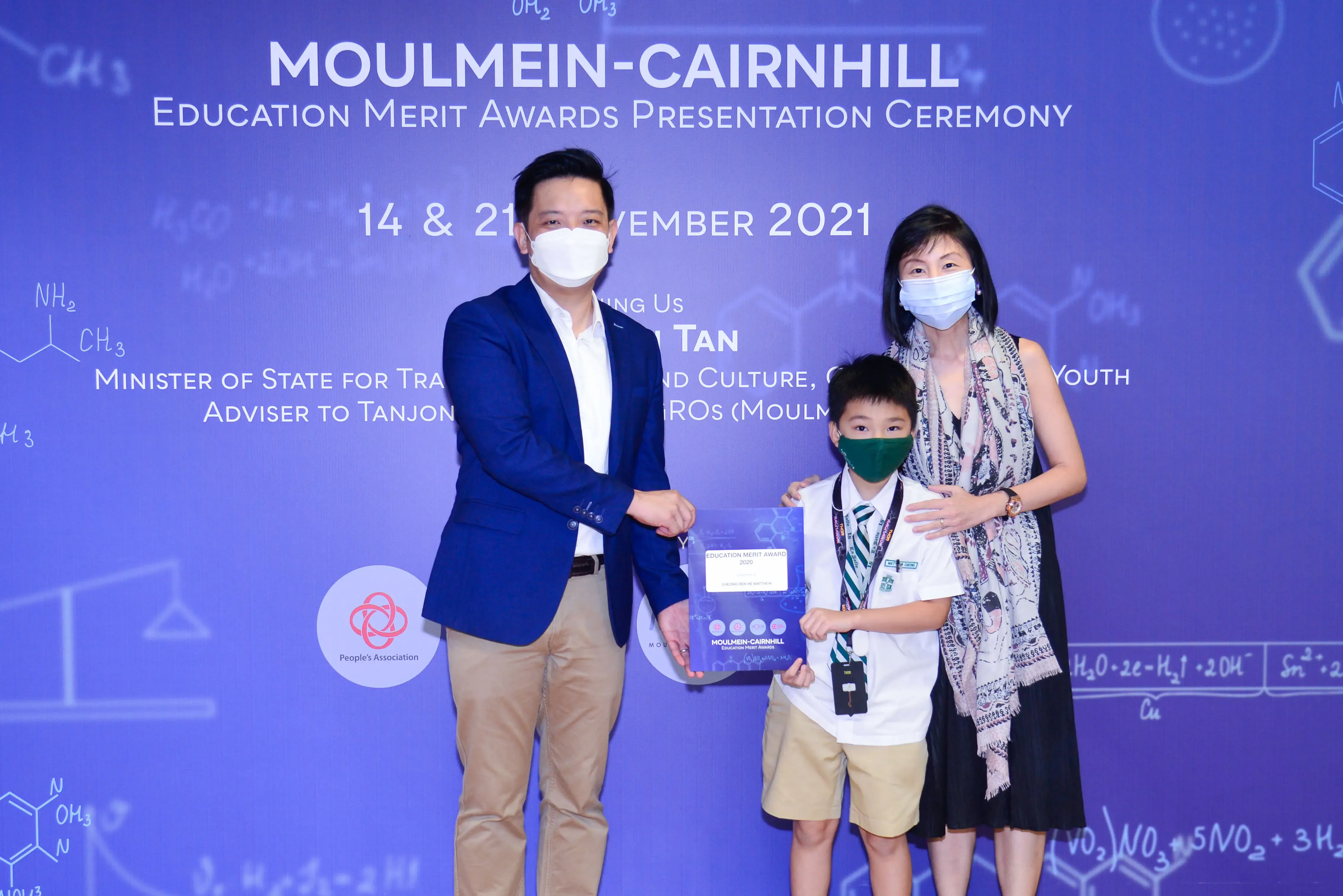 Two masked adults and a masked boy hold an award plaque at the Moulmein-Cairnhill Education Merit Awards 2021.