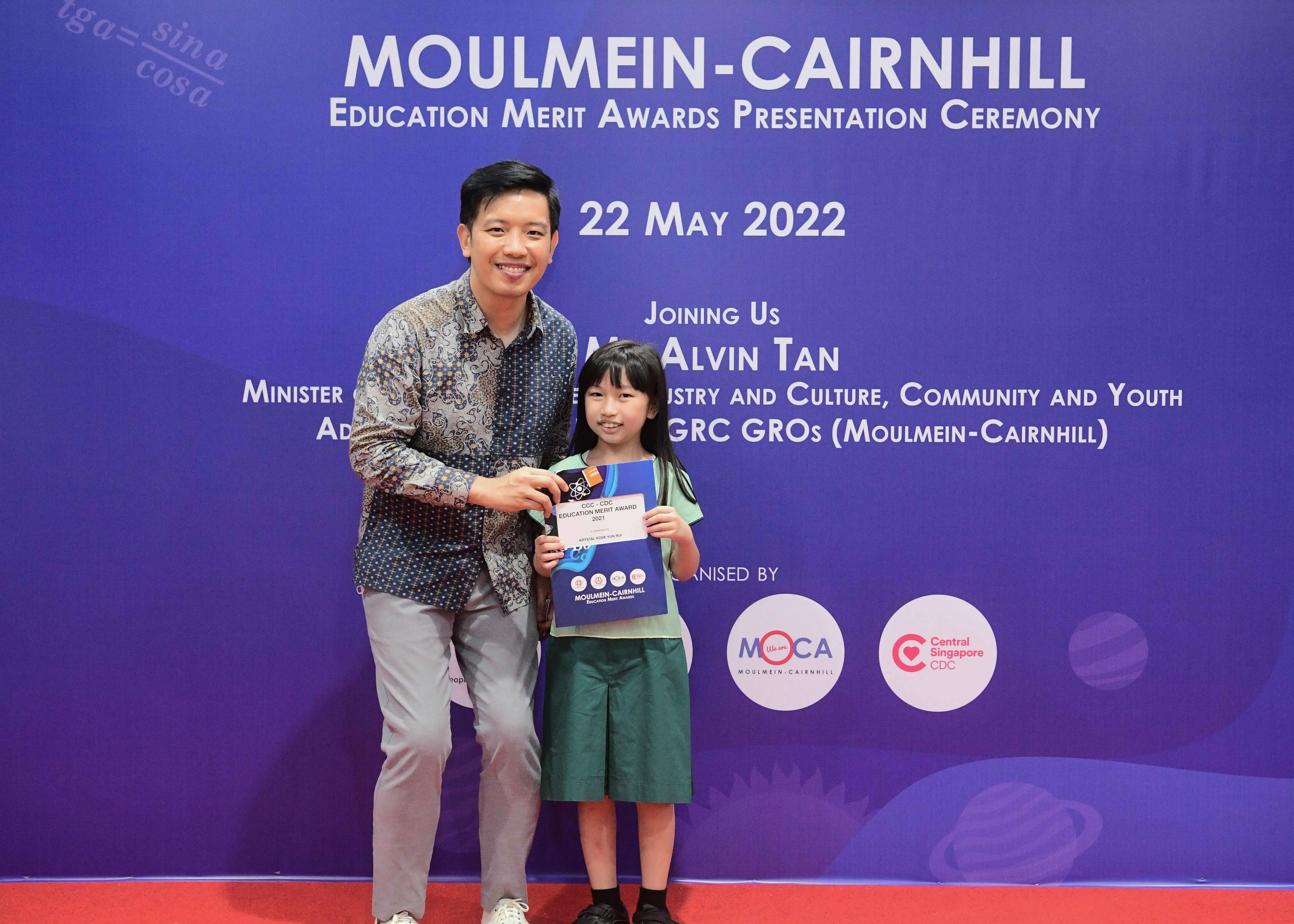 A man and a young girl pose together holding an award certificate at the Moulmein-Cairnhill Education Merit Awards on 22 May 2022.