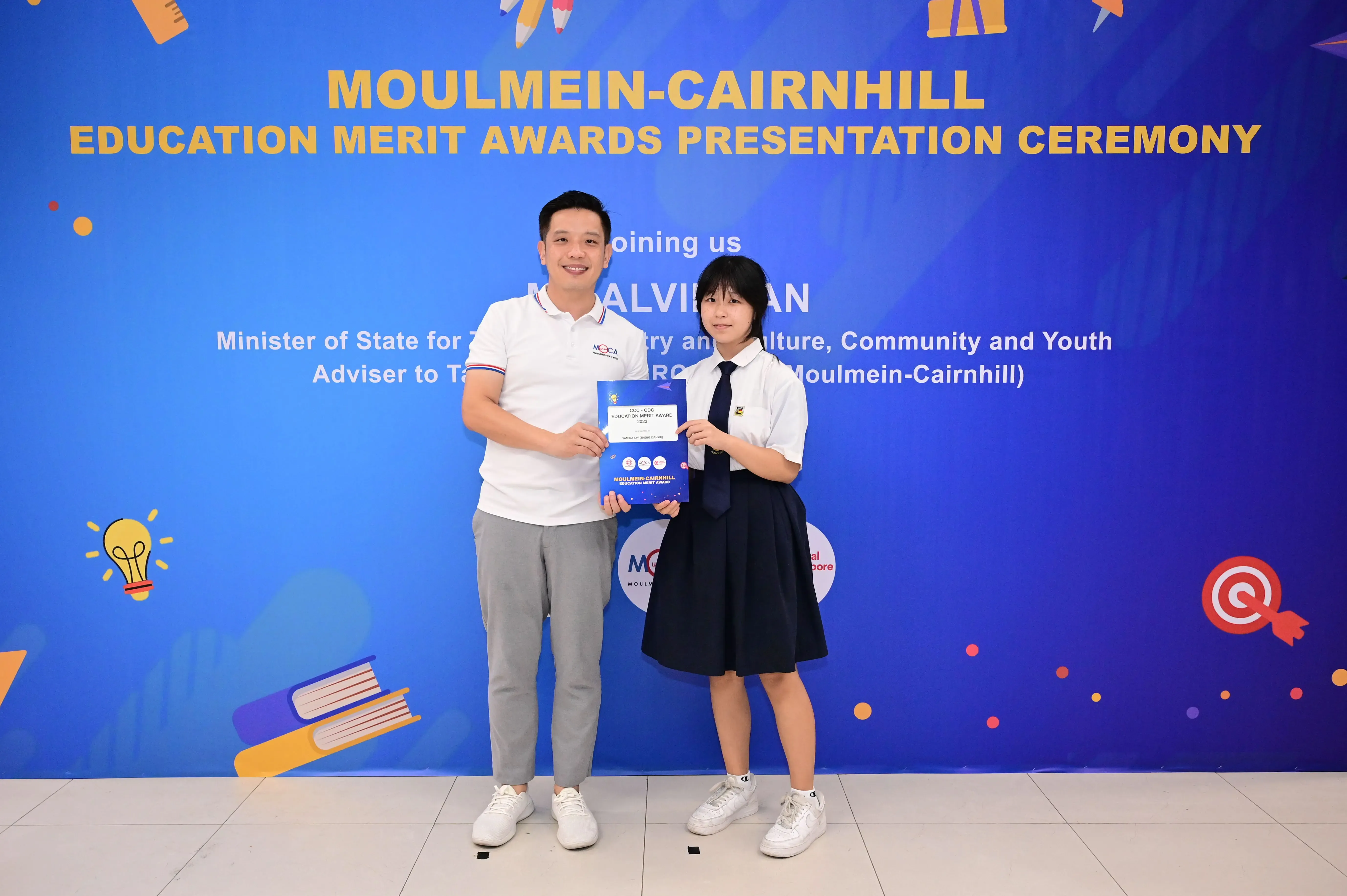 A man and a student in school uniform hold an award certificate at the Moulmein-Cairnhill Education Merit Awards ceremony.
