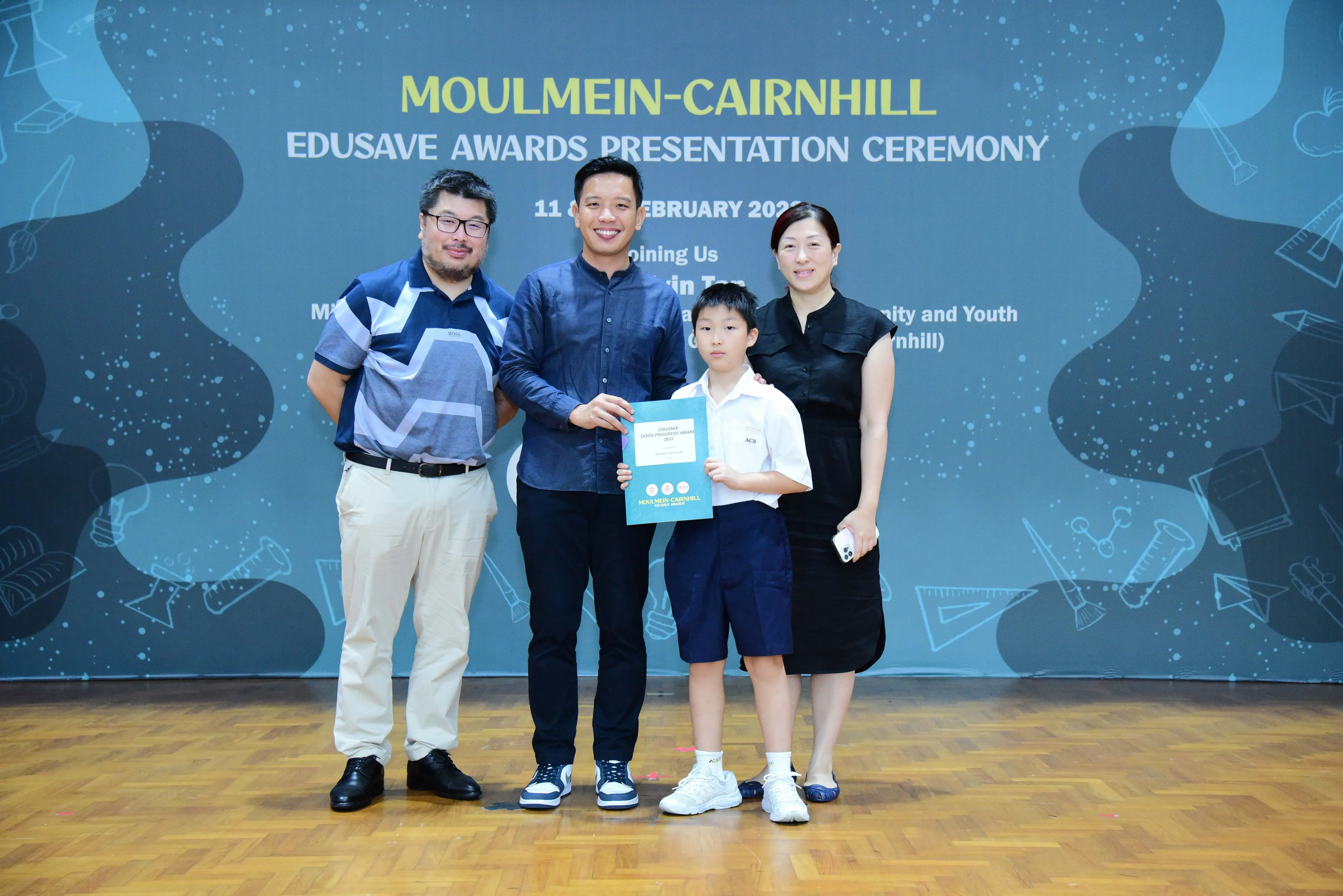 Three adults and a young boy pose holding a certificate at the Moulmein-Cairnhill Edusave Awards Presentation Ceremony.