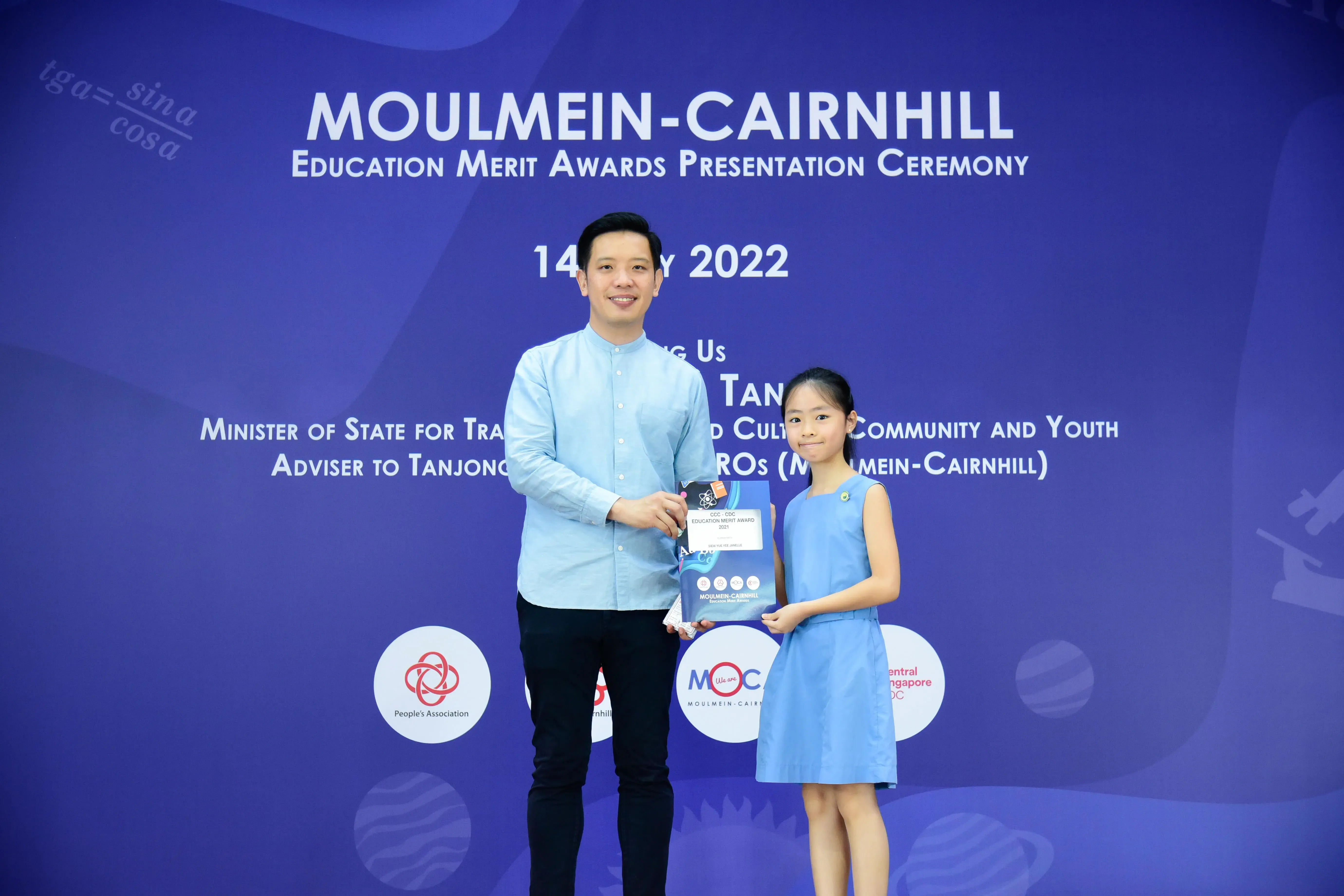 A man and a young girl in blue outfits hold an award at the Moulmein-Cairnhill Education Merit Awards 2022.