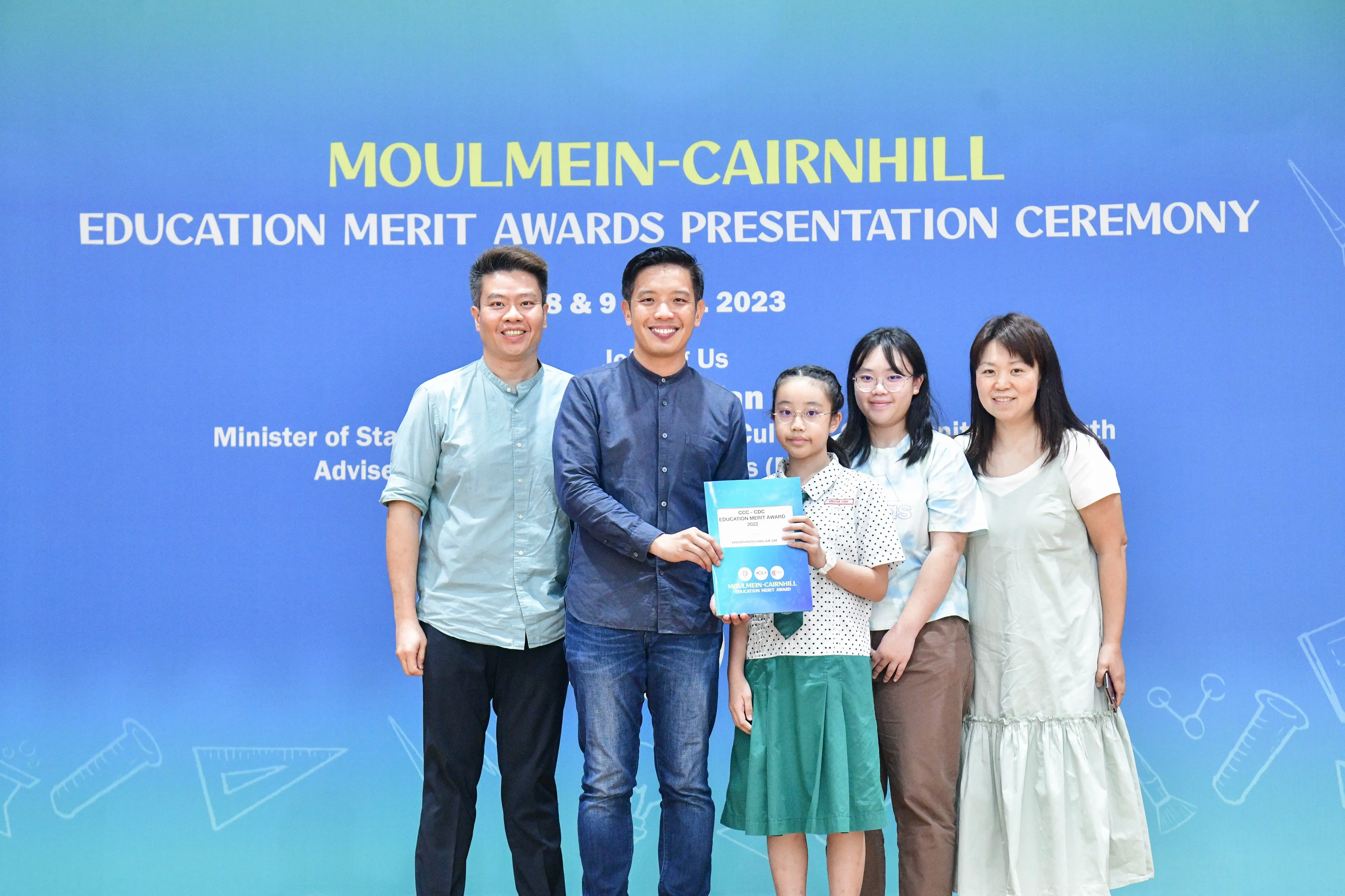 Five people pose at the Moulmein-Cairnhill Education Merit Awards Presentation Ceremony 2023, with a girl holding an award.