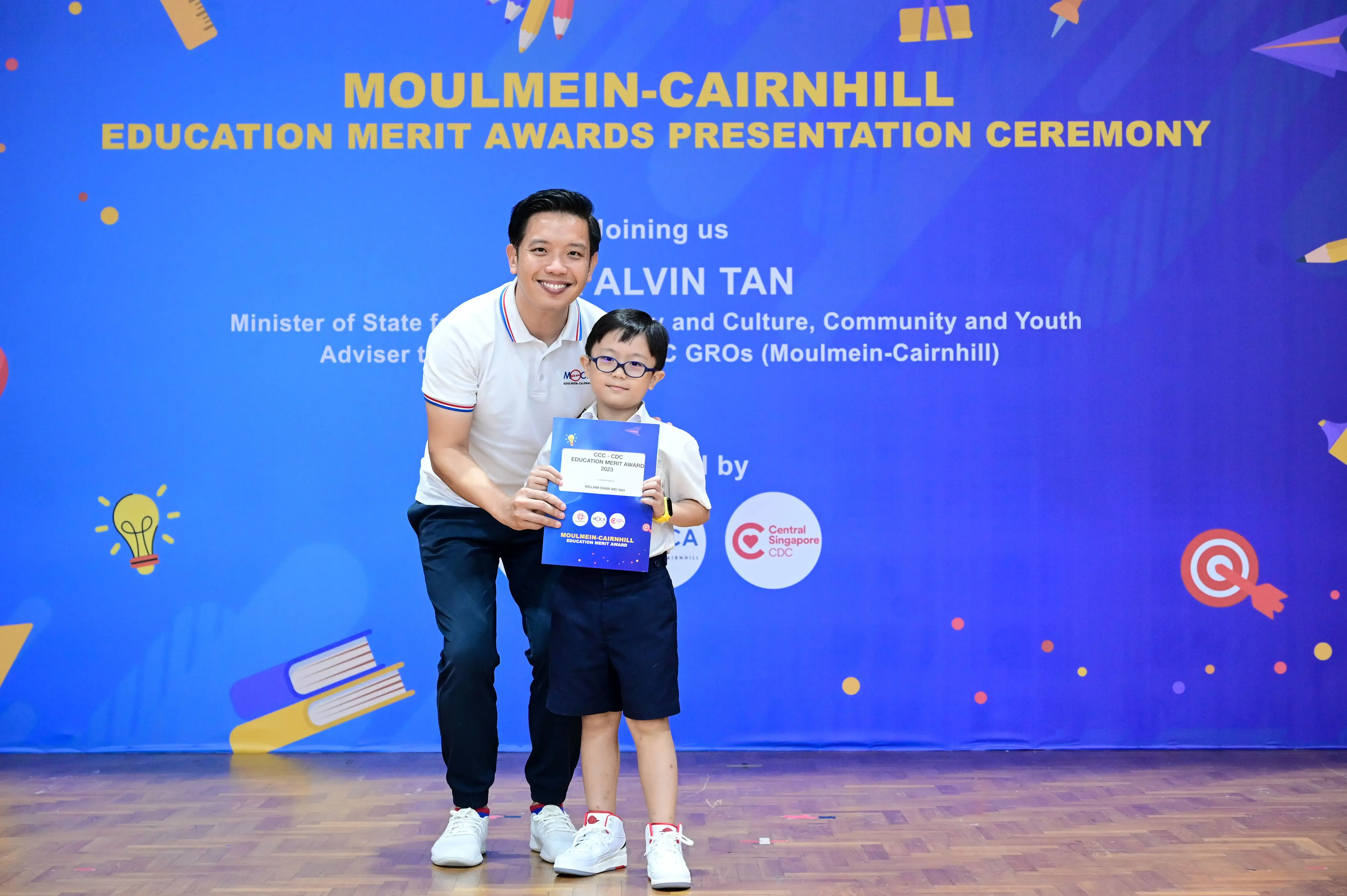 A man and a young boy holding an award certificate at the Moulmein-Cairnhill Education Merit Awards Ceremony.