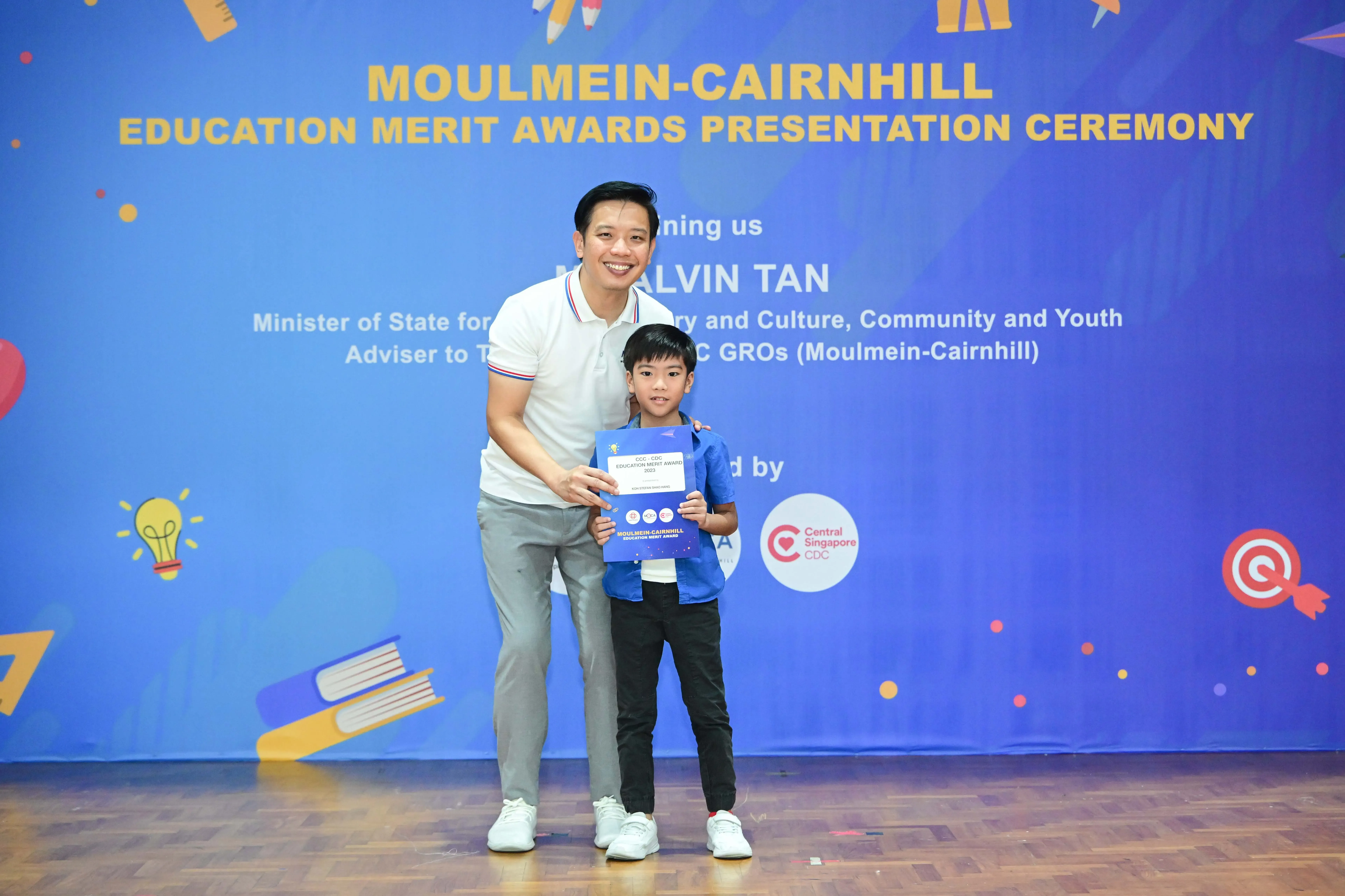 Man and young boy pose together holding a certificate at Moulmein-Cairnhill Education Merit Awards Ceremony.