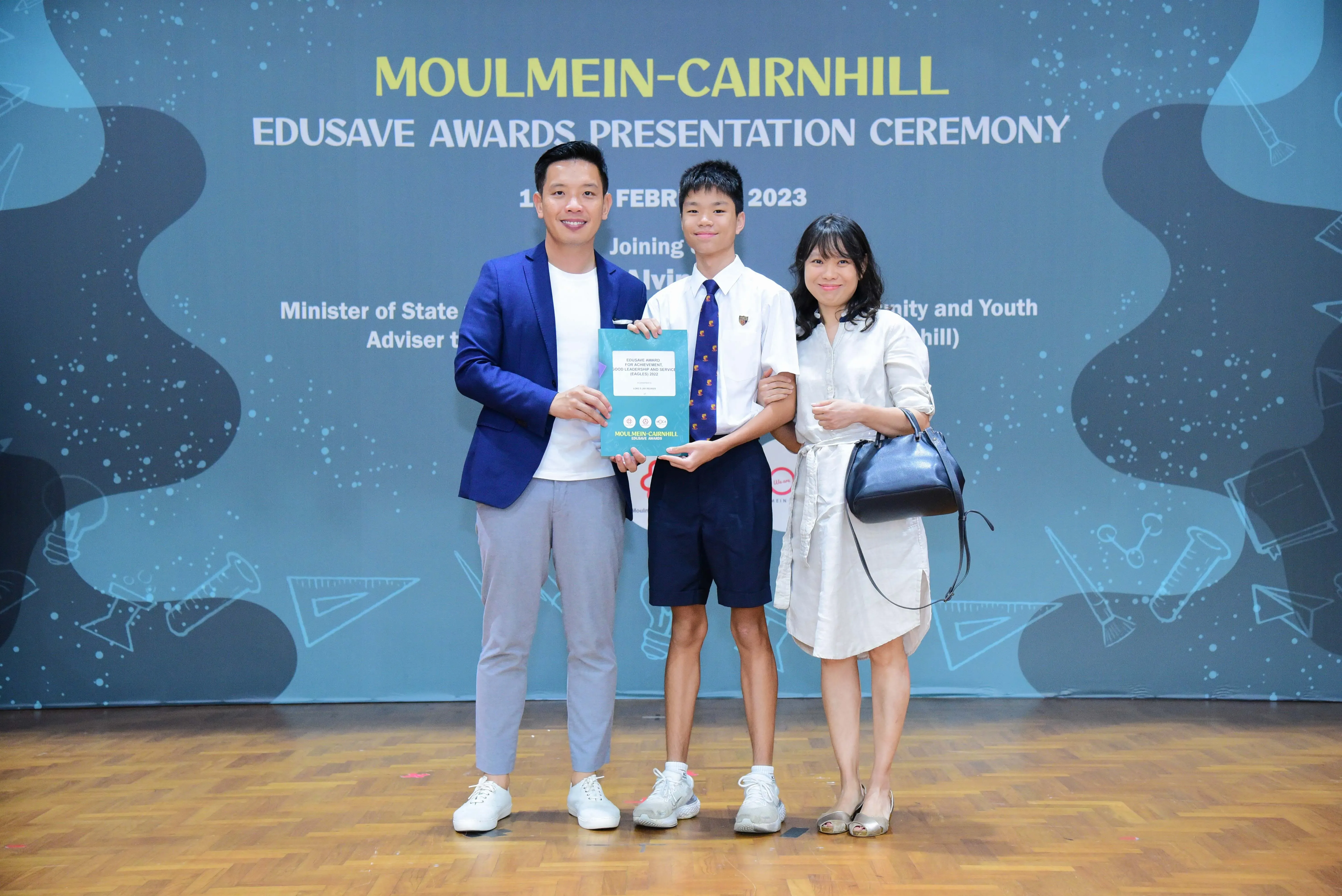 Three people pose at the Moulmein-Cairnhill Edusave Awards Presentation Ceremony 2023, with a student holding an award.