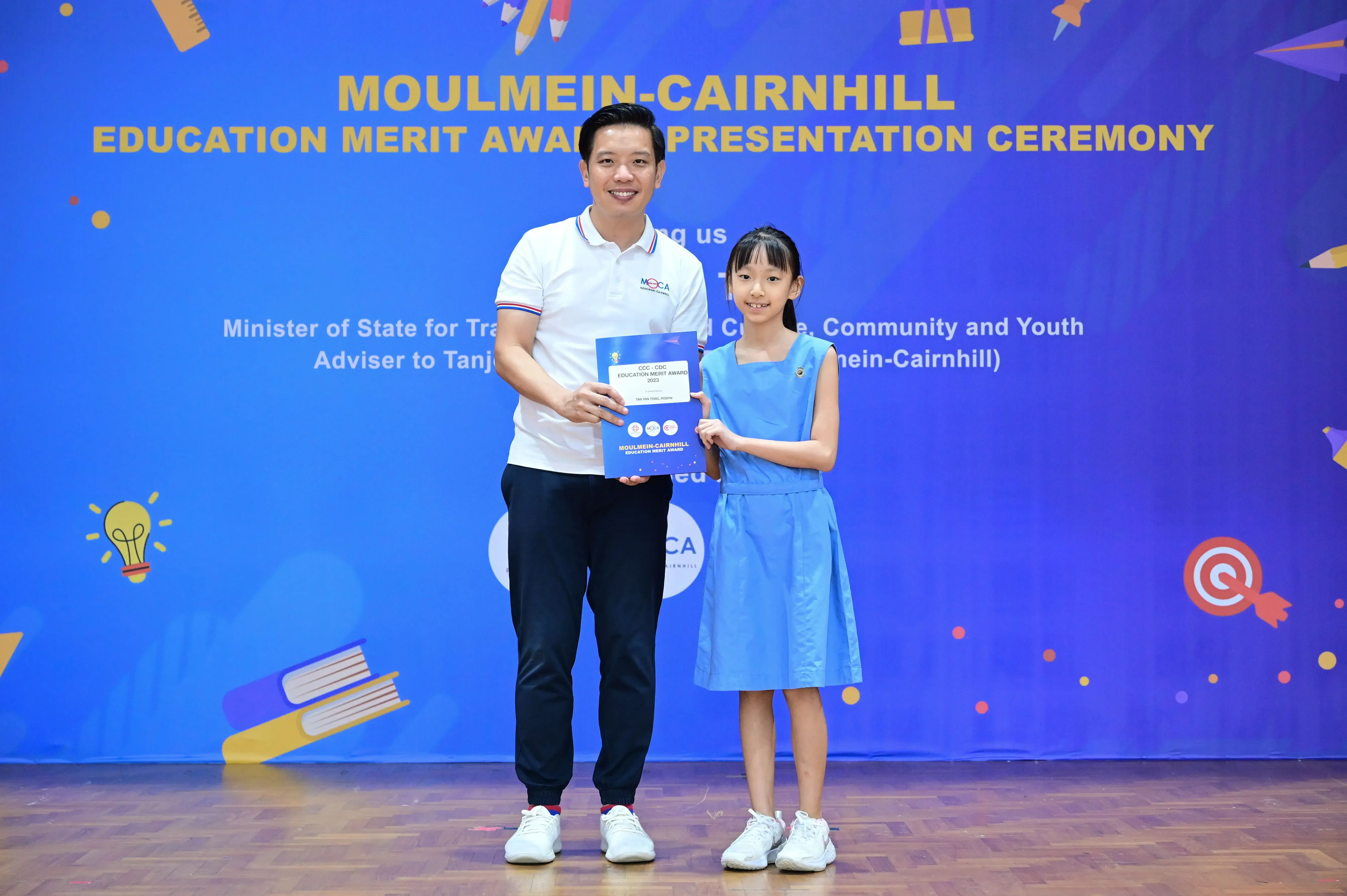 Man and young girl hold a certificate together at Moulmein-Cairnhill Education Merit Award Presentation Ceremony.