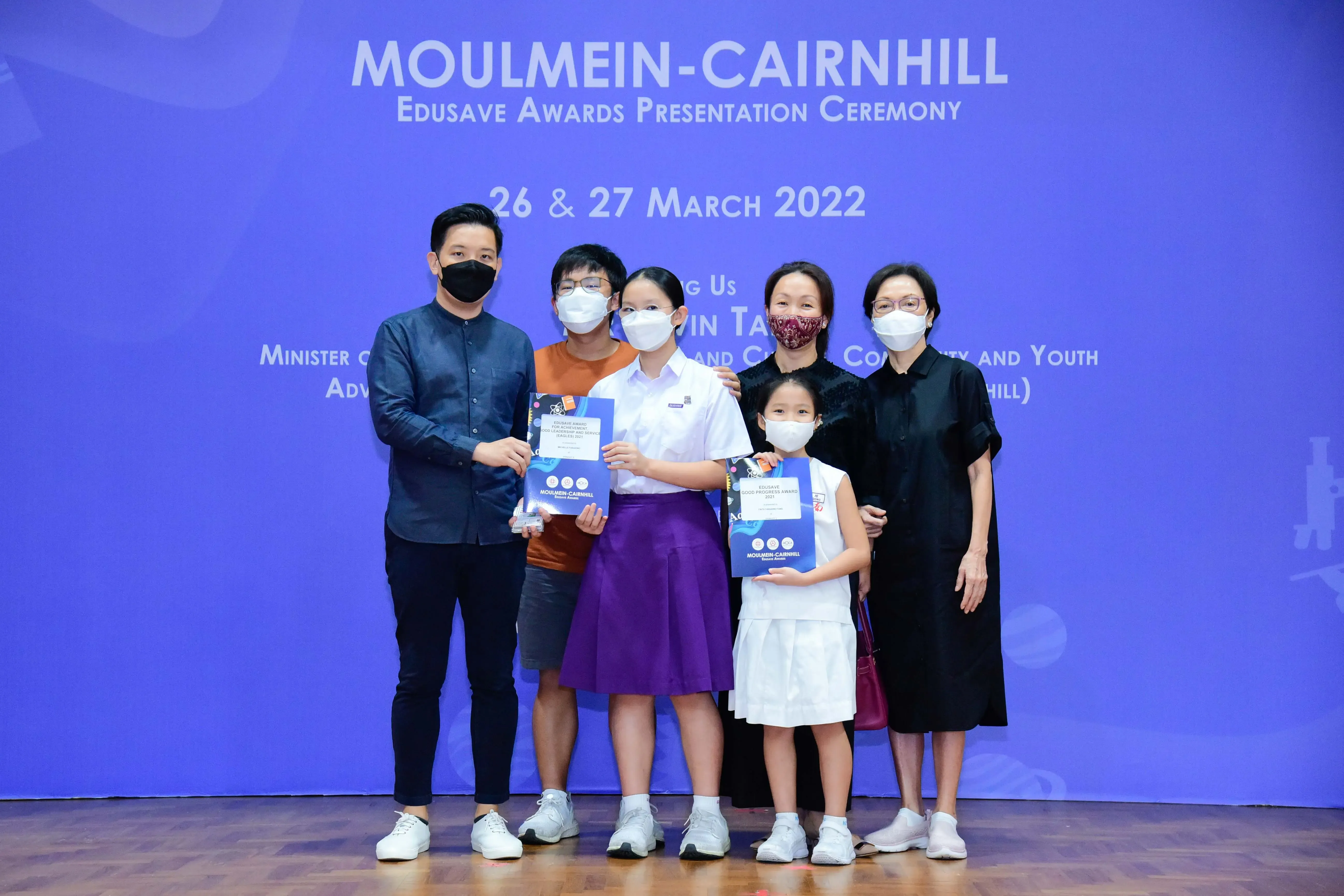 Six masked people pose with awards at the Moulmein-Cairnhill Edusave Awards Presentation Ceremony, March 2022.