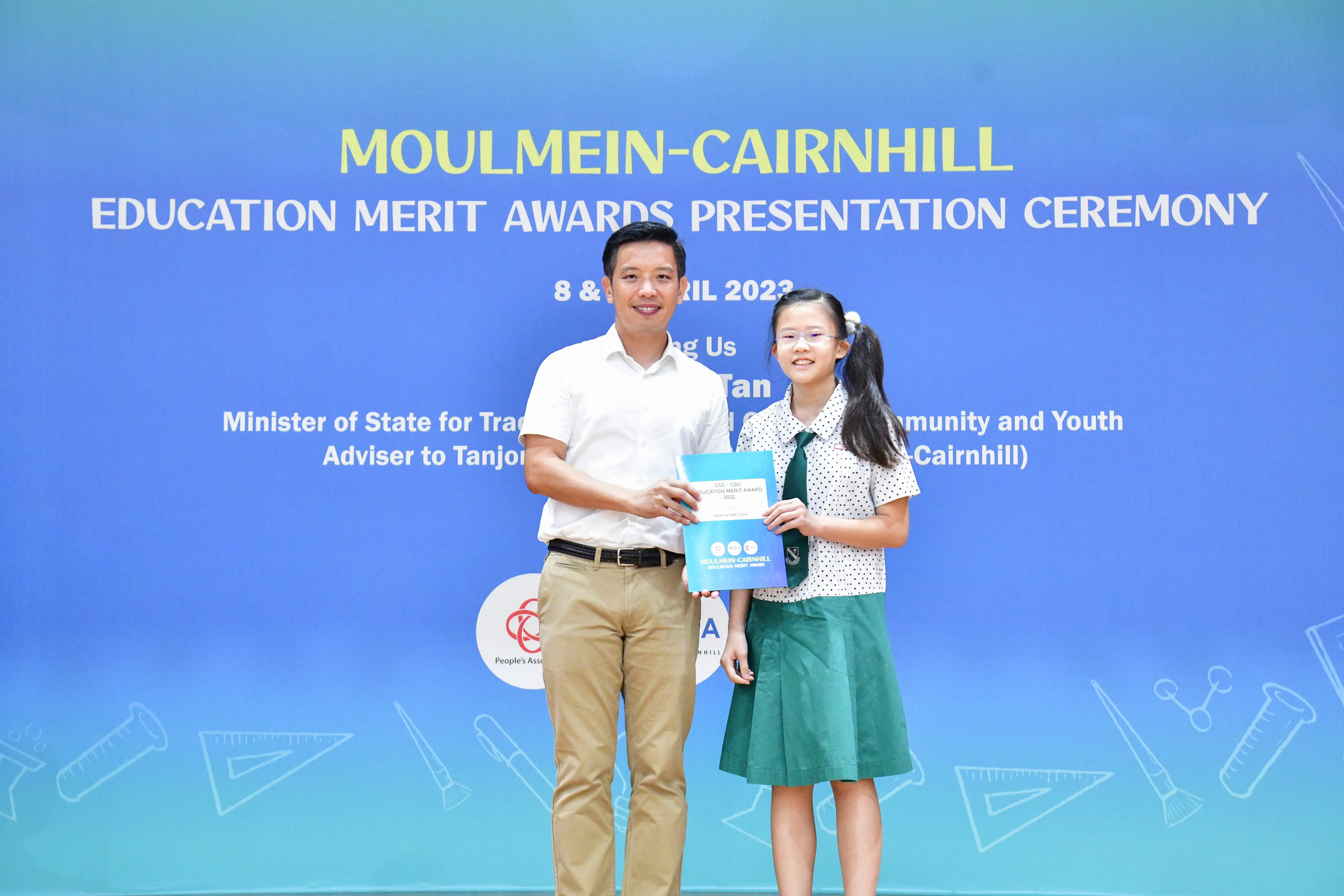 A man and a young girl in school uniform hold an award certificate at the Moulmein-Cairnhill Education Merit Awards ceremony.