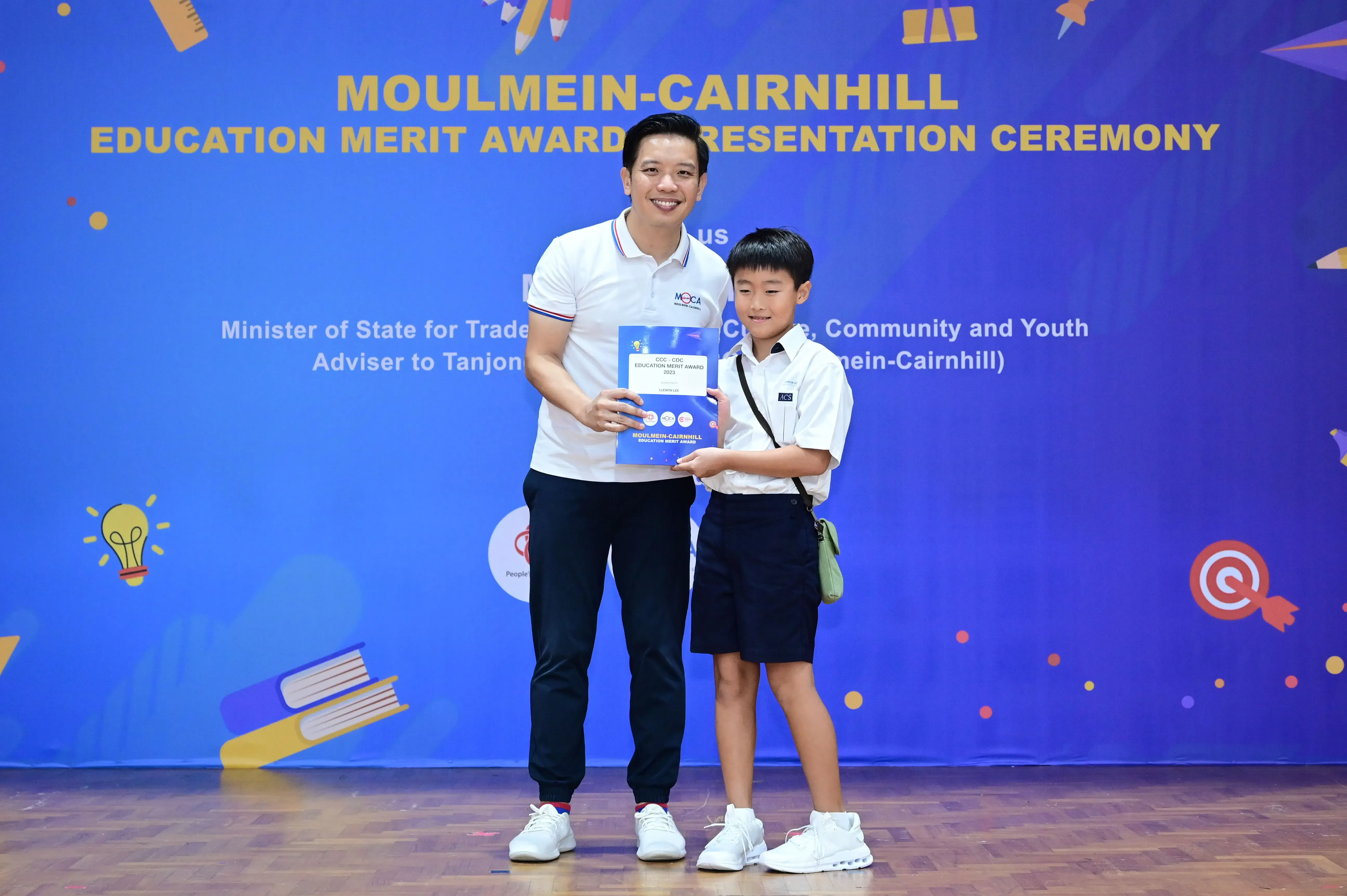 An adult and a young boy hold an award certificate at the Moulmein-Cairnhill Education Merit Award Presentation Ceremony.