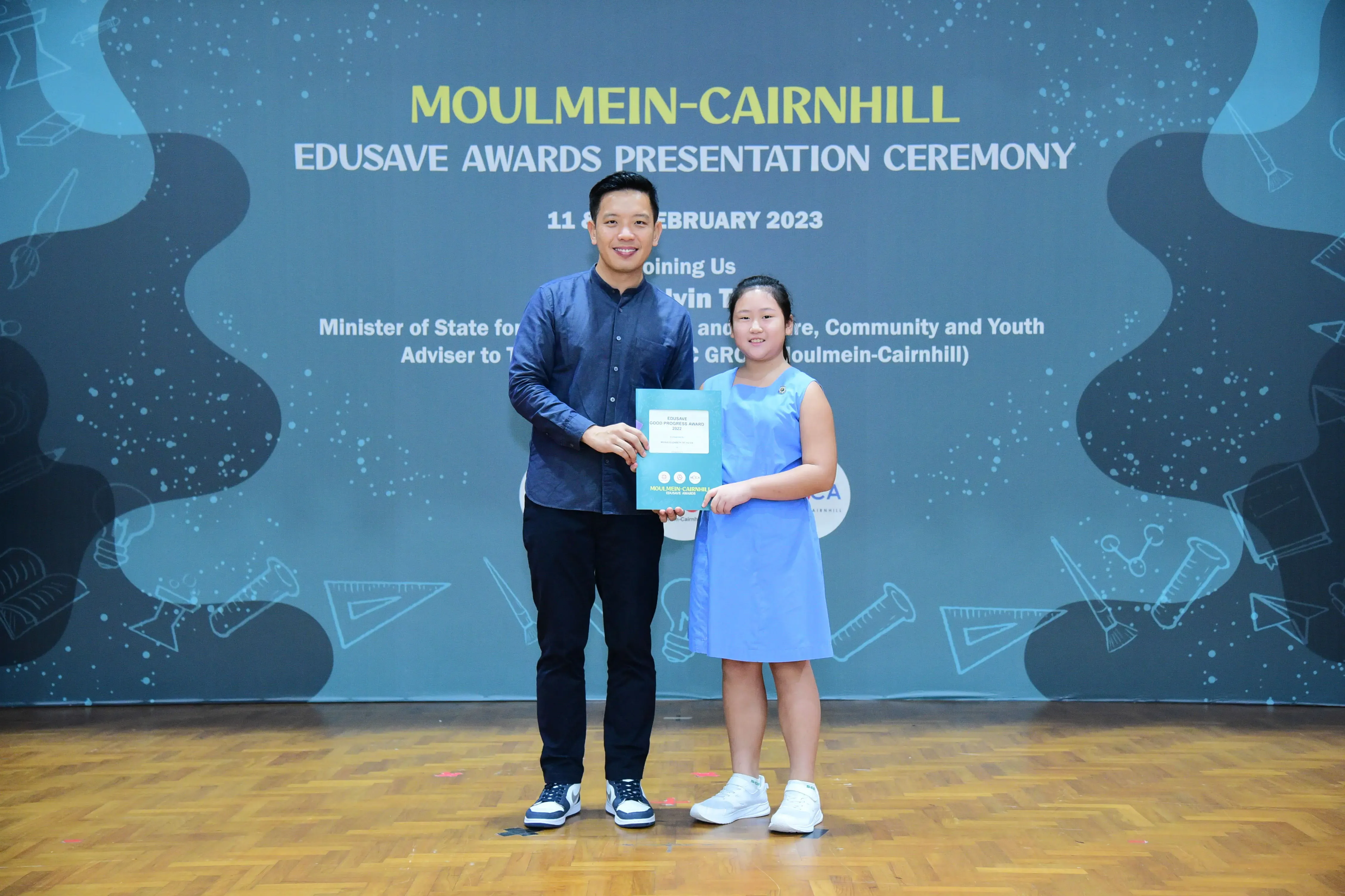 A man and a young girl hold a certificate at the Moulmein-Cairnhill Edusave Awards Presentation Ceremony 2023.