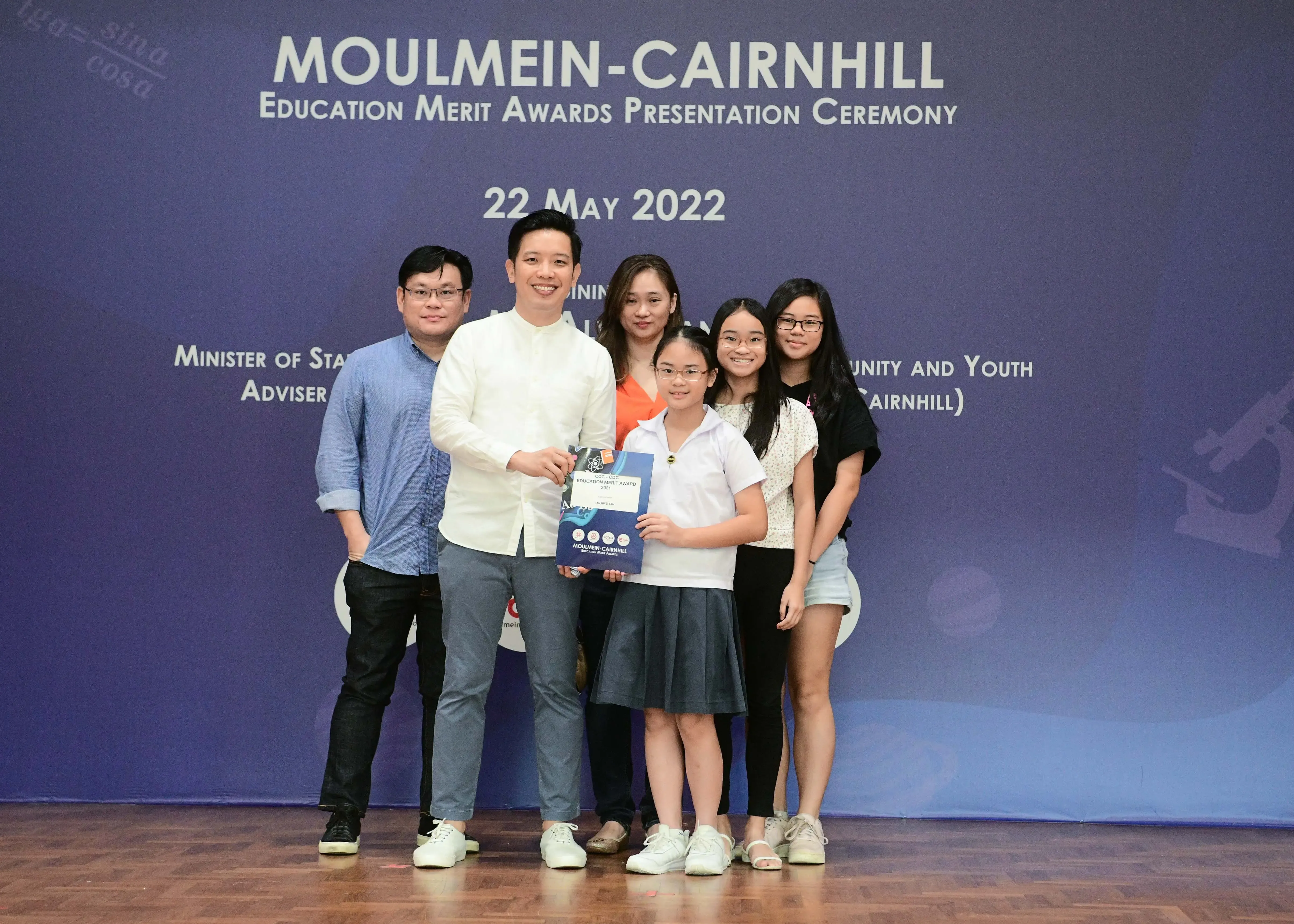 Five people pose with a young girl holding an award certificate at the Moulmein-Cairnhill Education Merit Awards on 22 May 2022.