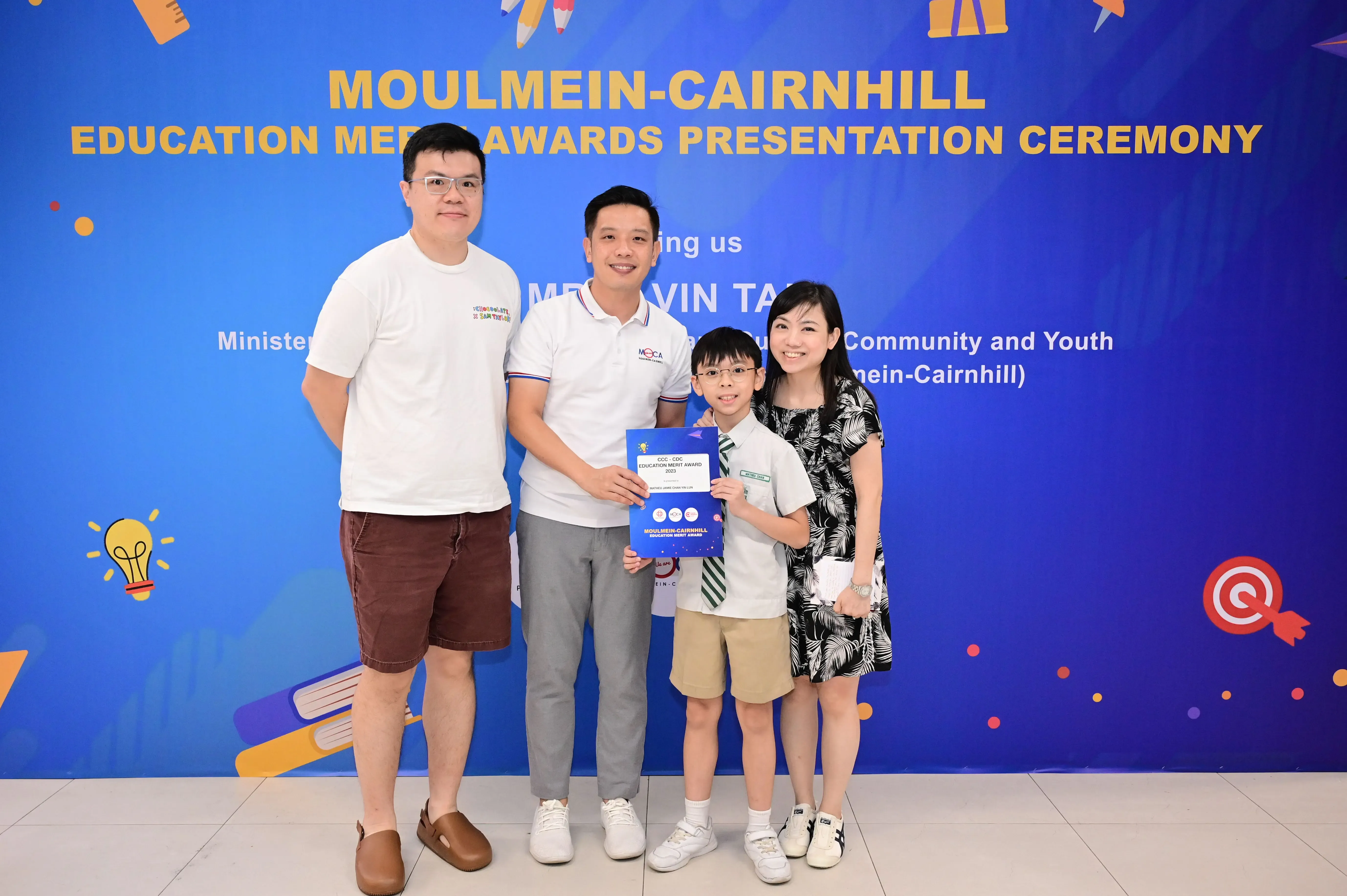 Three adults and a boy holding an award certificate pose at the Moulmein-Cairnhill Education Merit Awards ceremony.